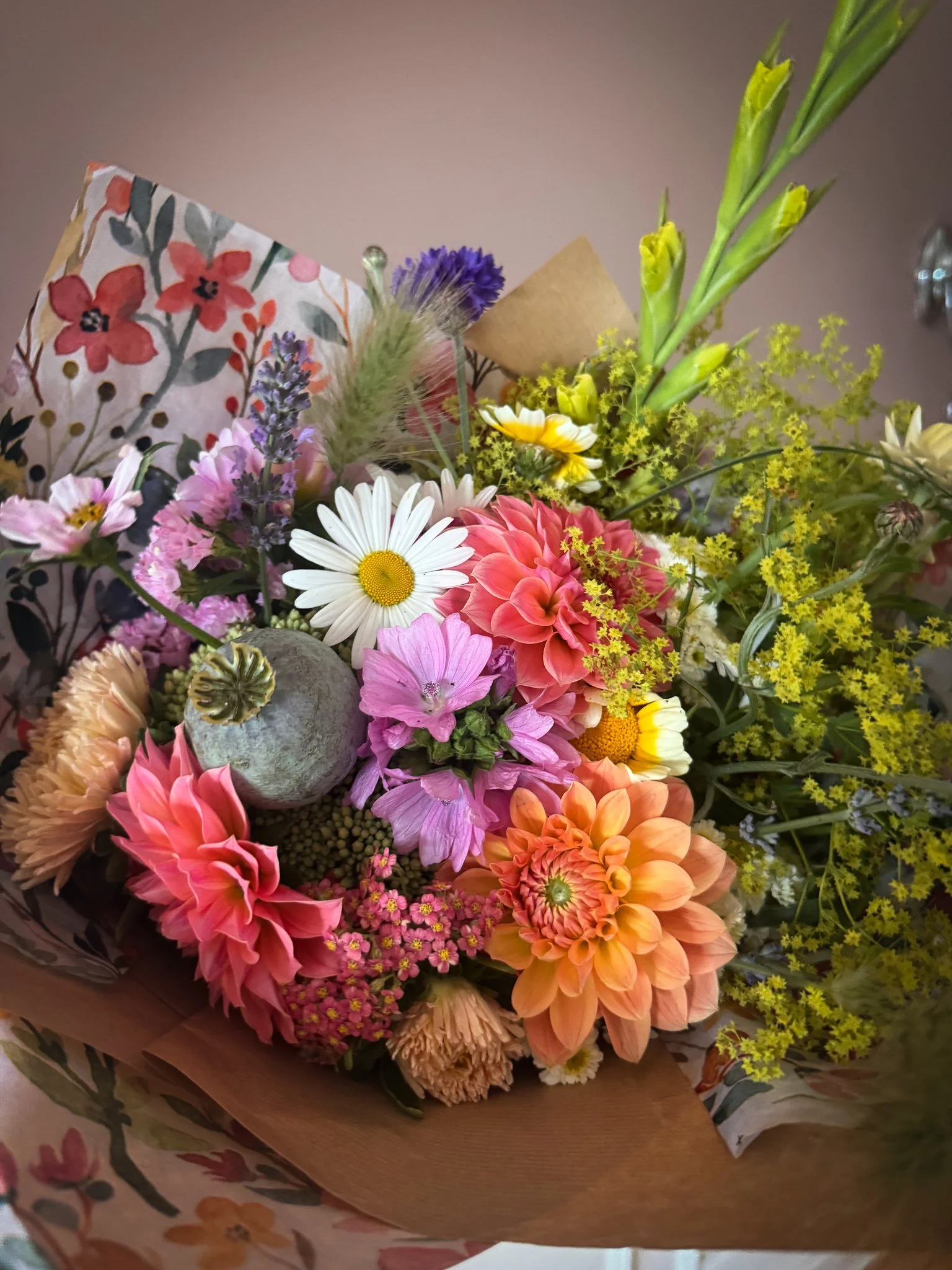 Colorful bouquet of mixed flowers including daisies, dahlias, snapdragons, and various greenery, wrapped in decorative floral paper.