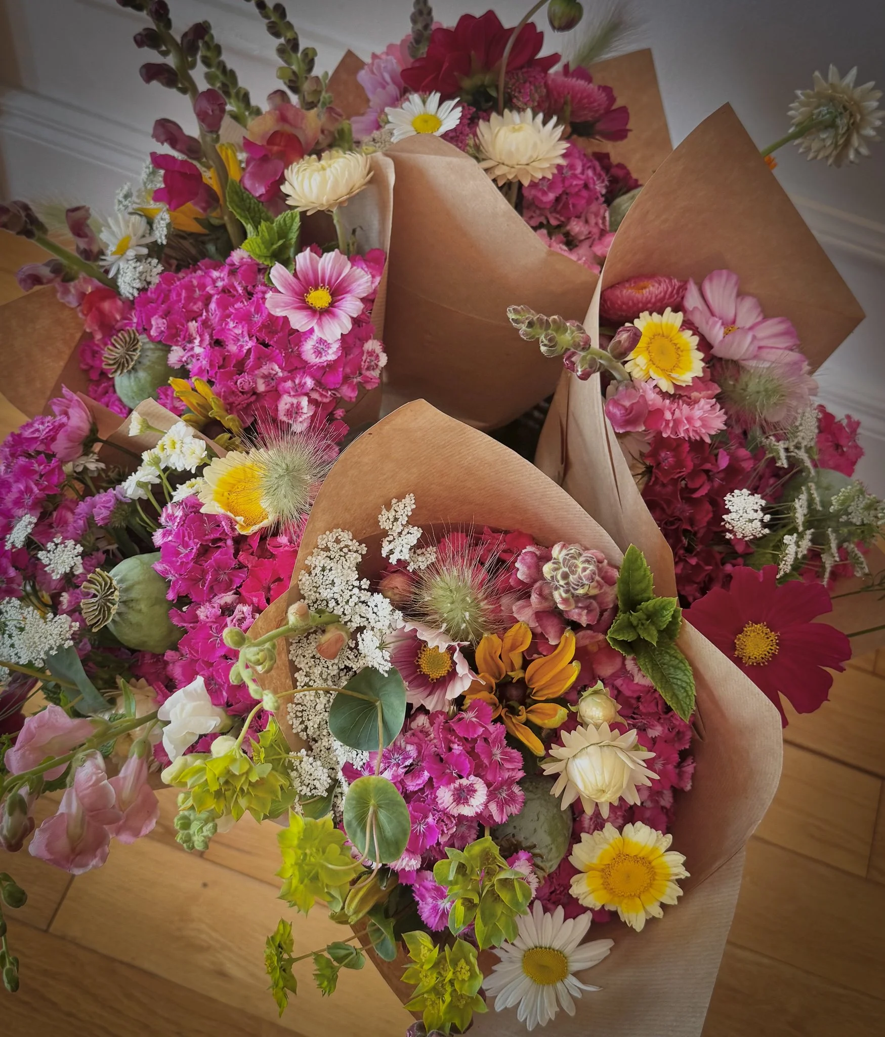 Colorful bouquets of pink, white, and yellow flowers wrapped in brown paper resting on a wooden floor.