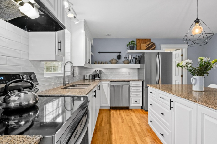 A image of a renovated kitchen, with white cupboards, black handles, stainless steel appliances and white backsplash.