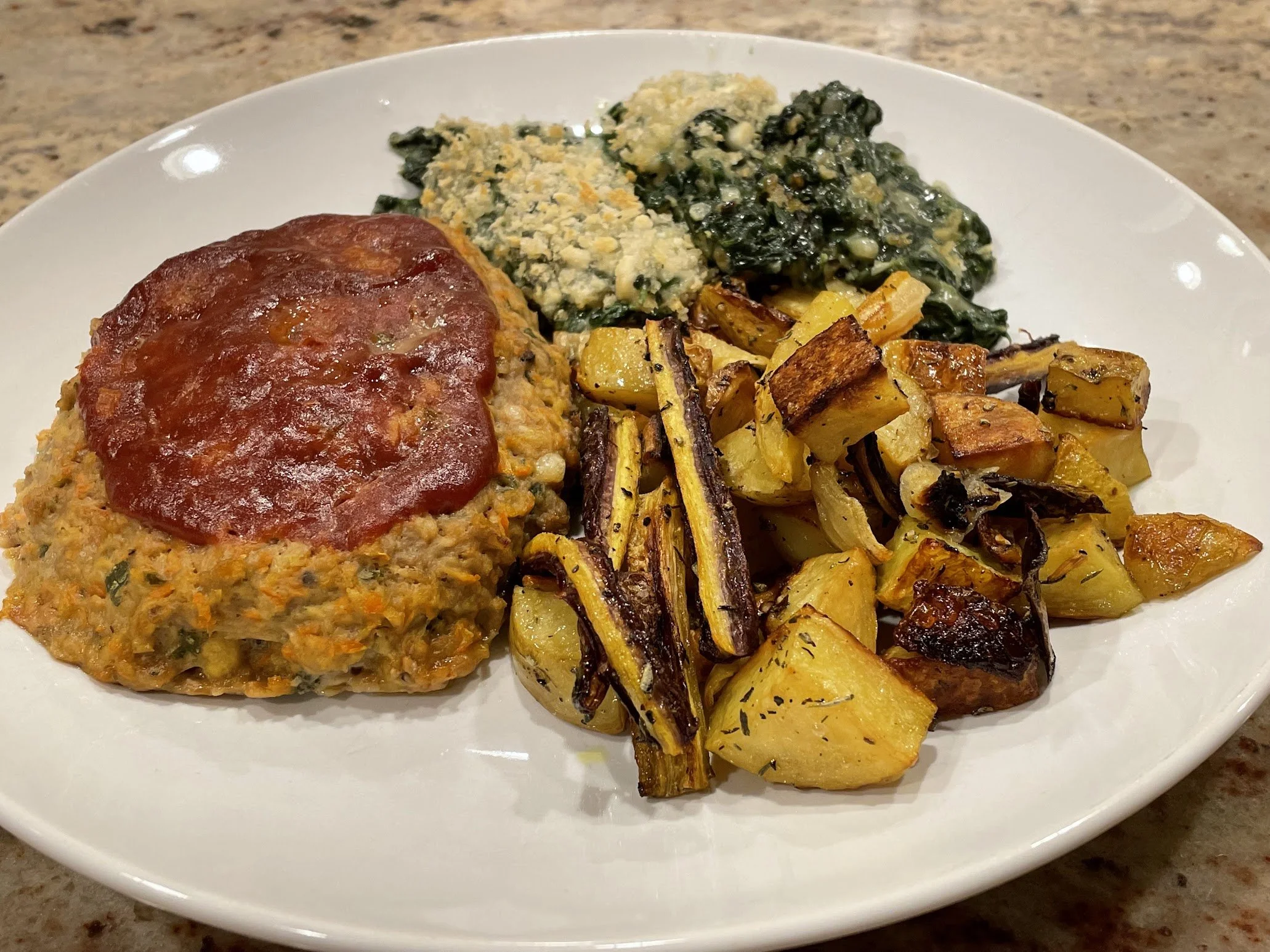 Plate with baked chicken topped with tomato sauce, mashed potatoes with spinach and cheese, roasted potatoes and onions.