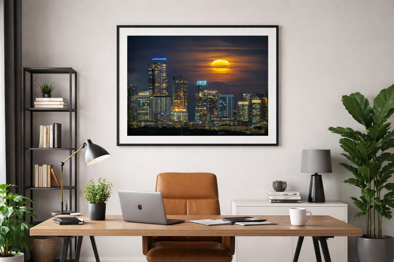 A modern office with a wooden desk, leather chair, laptop, and desk lamp, with framed cityscape photo on wall showing skyscrapers and a moonlit sky.