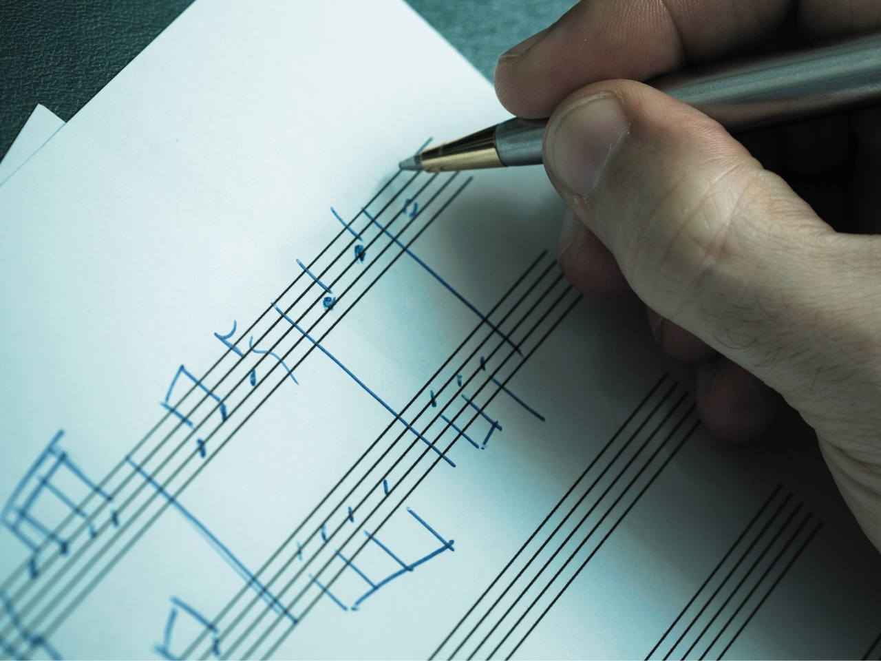 A person writing musical notation on sheet music with a pen.