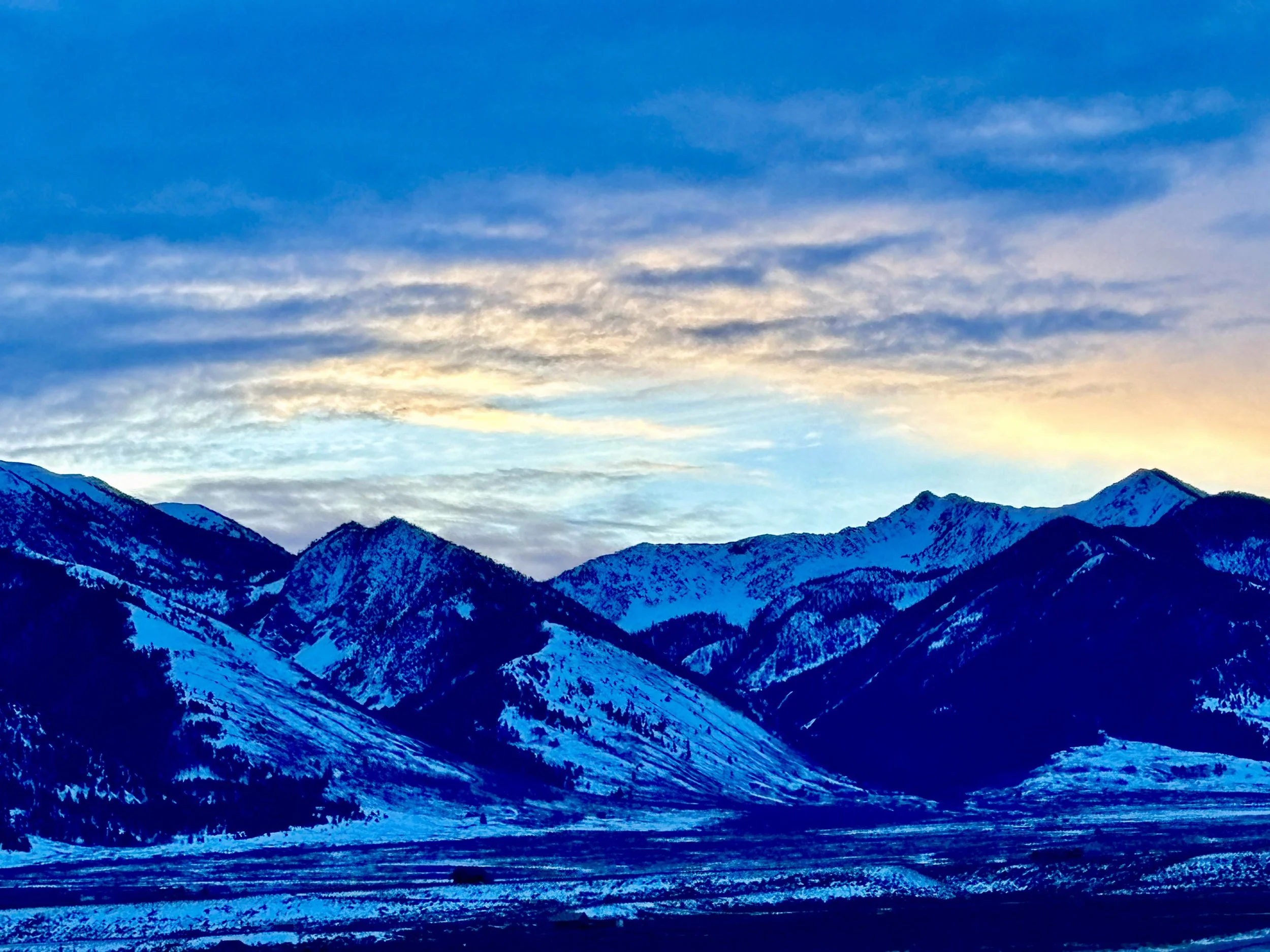 Snow-covered mountains under a colorful sky at sunset or sunrise.