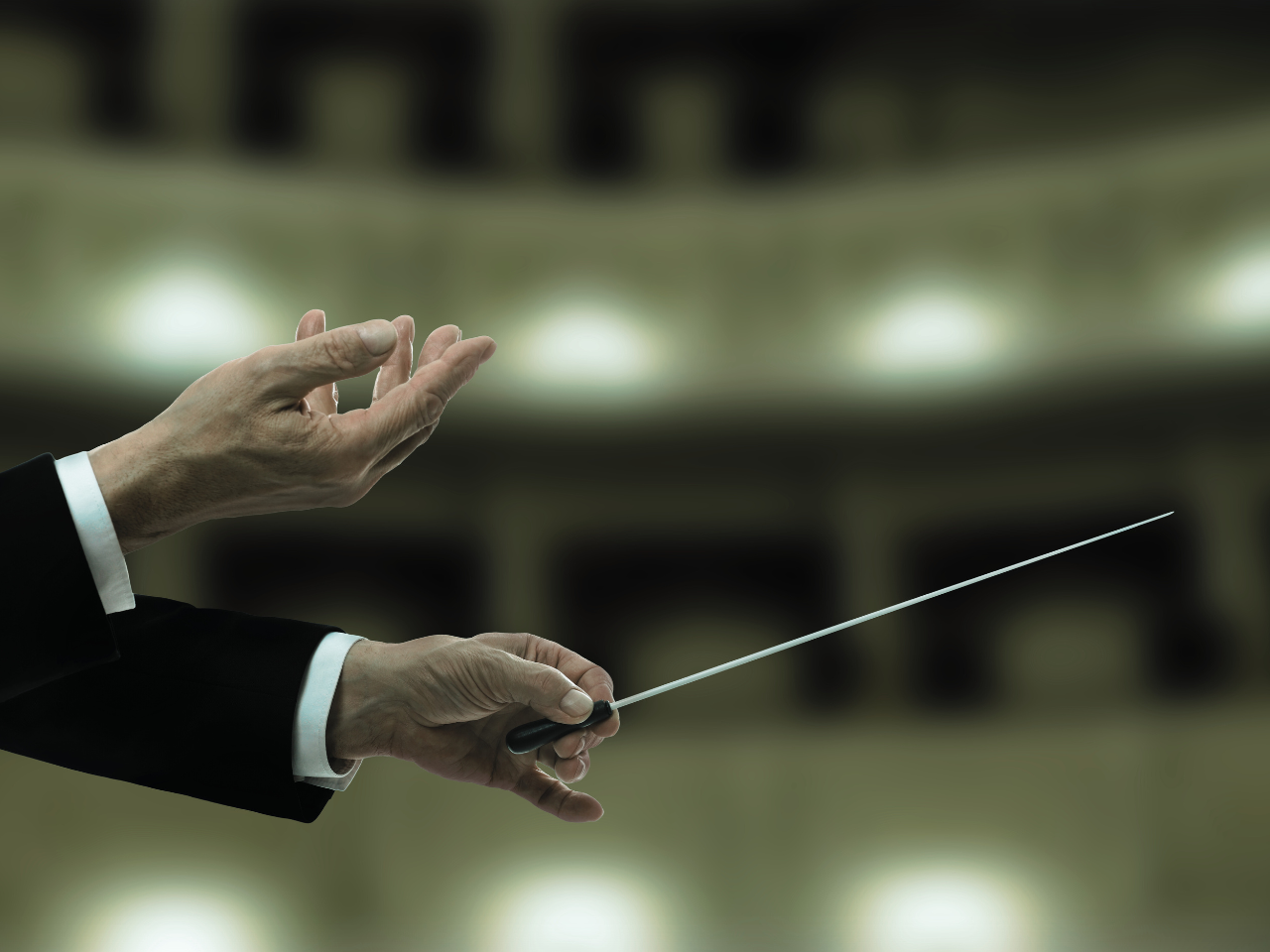 A person in a suit conducting an orchestra with a baton.