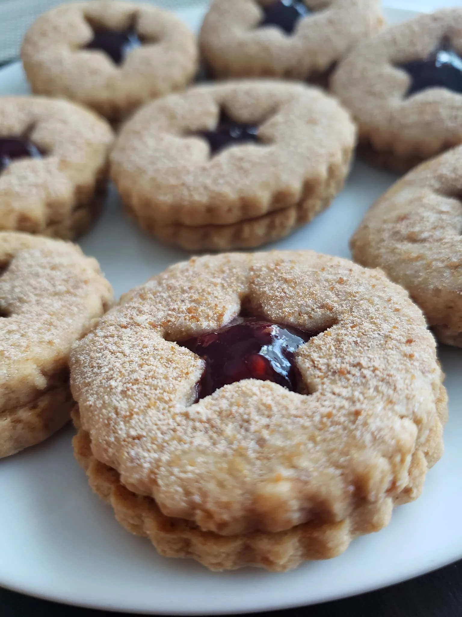 Close-up of thumbprint cookies with jam filling, dusted with powdered sugar on a white plate.