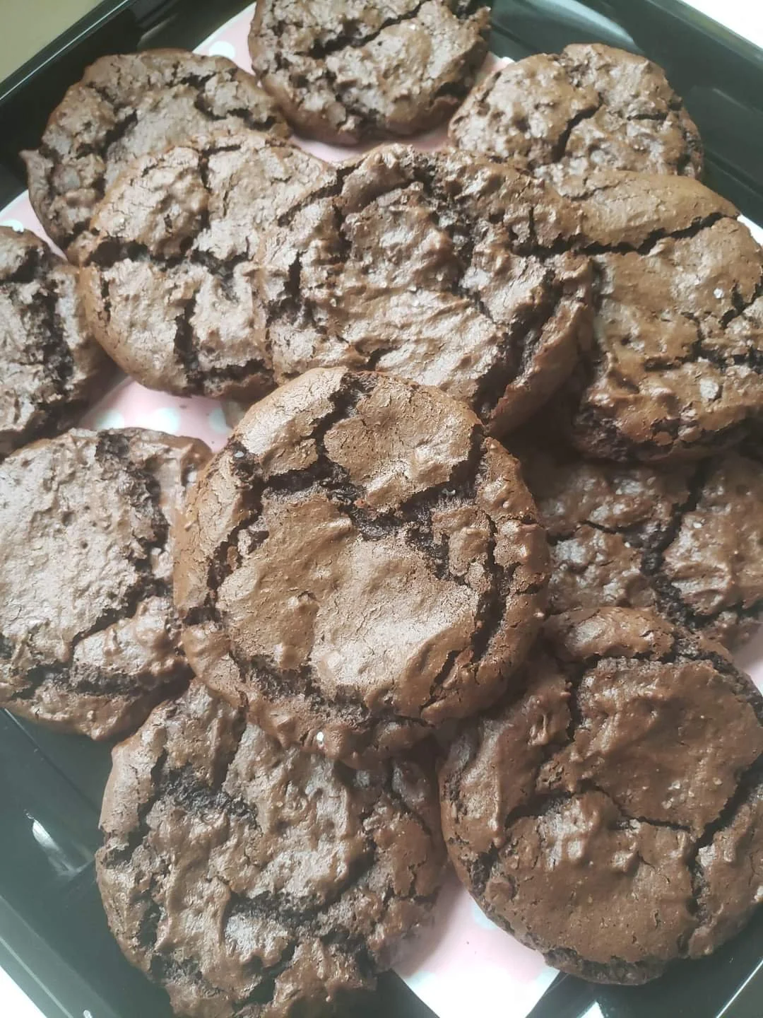 A tray of freshly baked chocolate crinkle cookies with a cracked surface and powdered sugar coating.