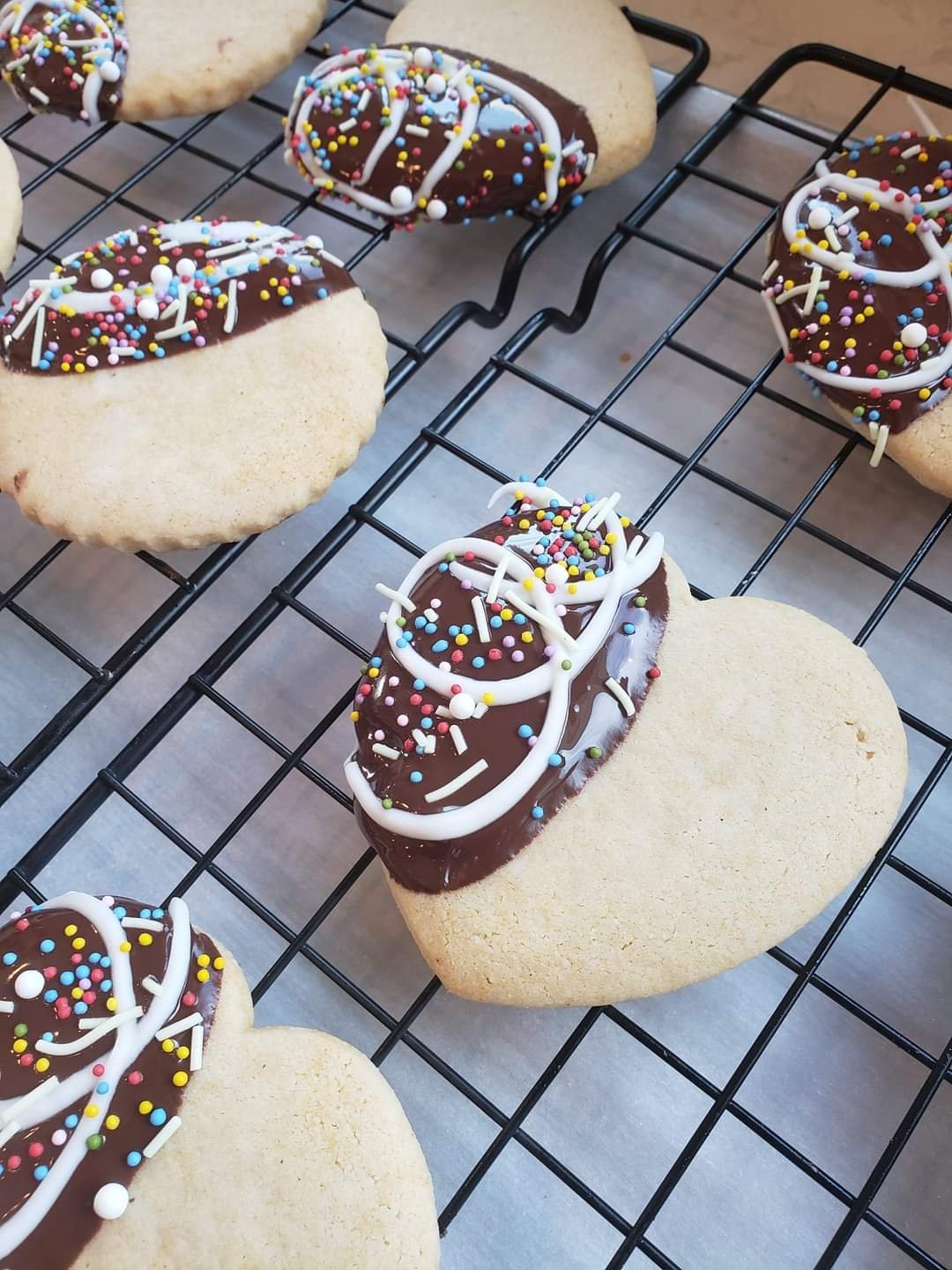 Decorated cookies with chocolate frosting and colorful sprinkles on black wire cooling rack.