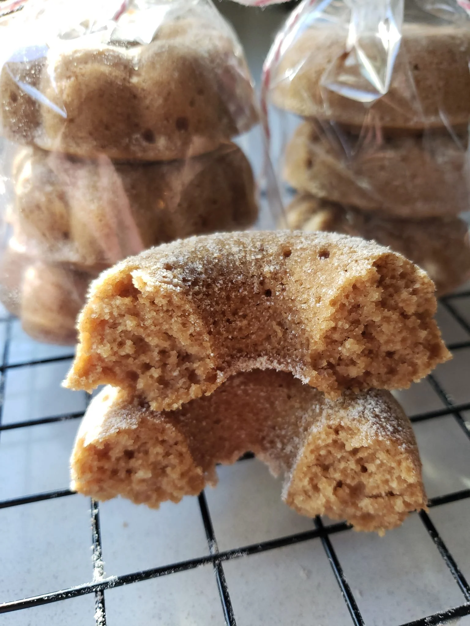 Close-up of a partially eaten cookie with a bite taken out, placed on a wire cooling rack. In the background, sealed plastic bags contain more cookies.