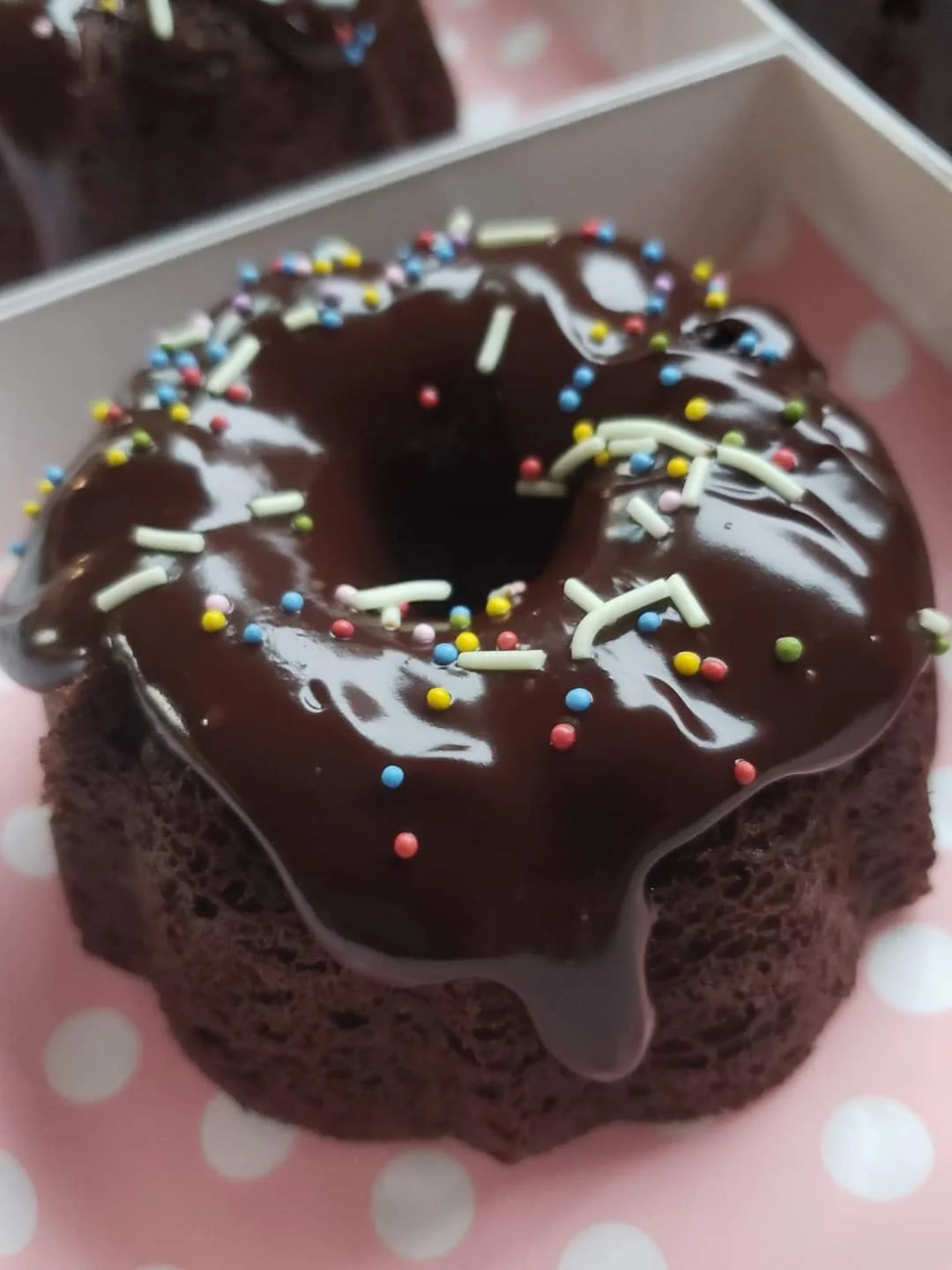 Chocolate donut with colorful sprinkles and white chocolate sticks on pink polka-dotted paper