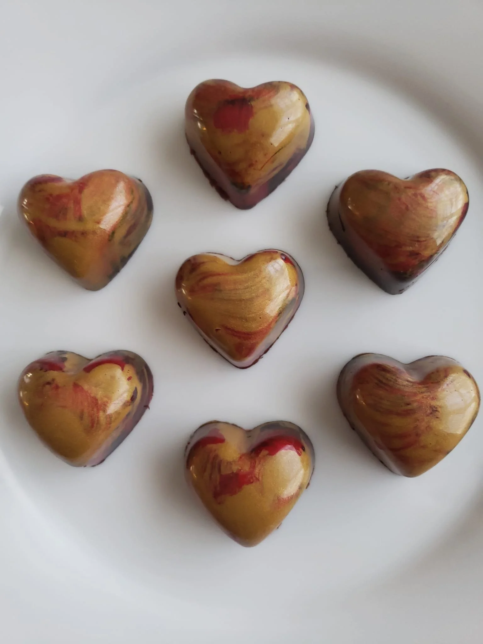 Seven heart-shaped chocolates with swirled brown, yellow, and red marbled patterns on a white plate.