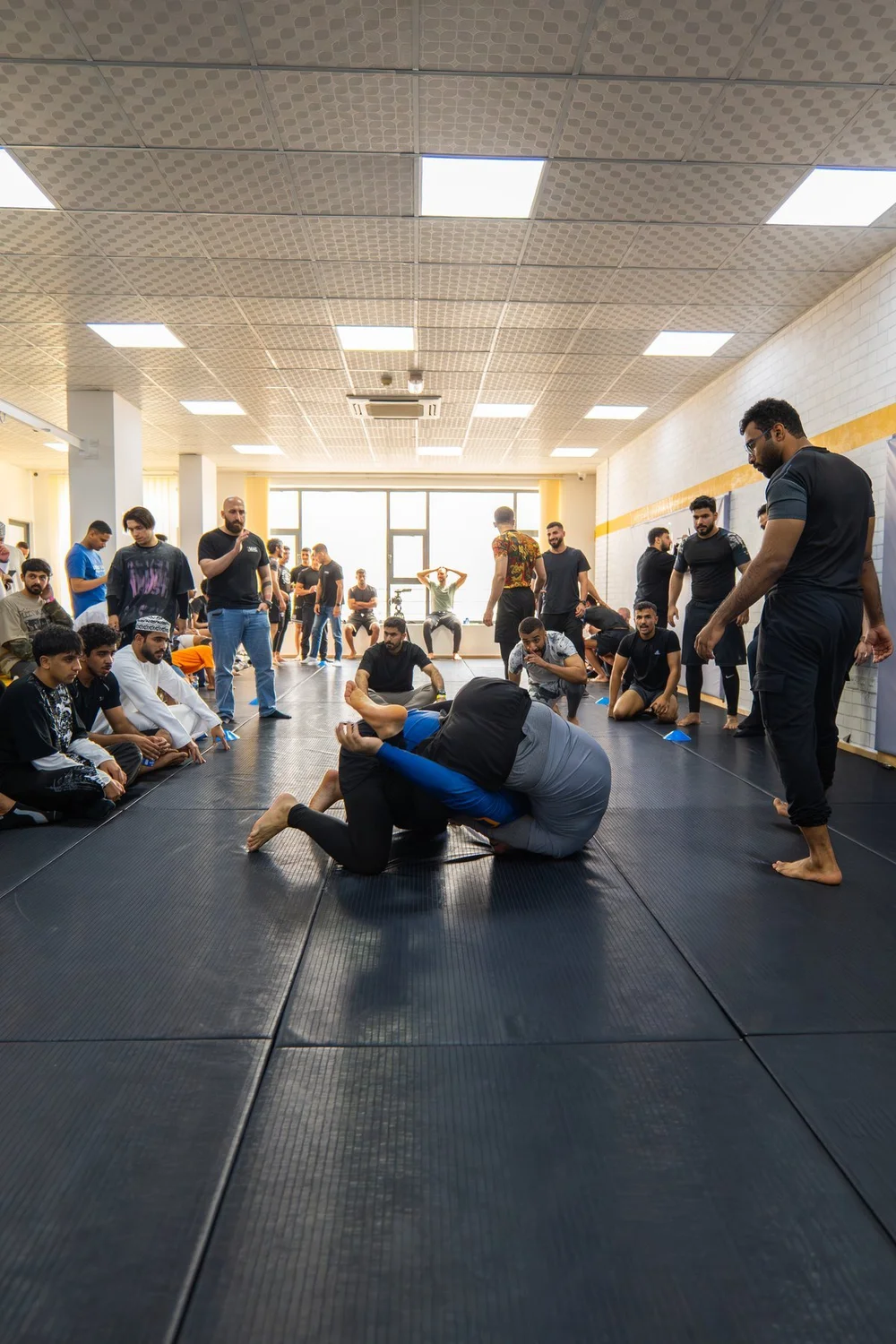 A coach demonstrating grappling while students watch on the mats at Fight Sports Muscat