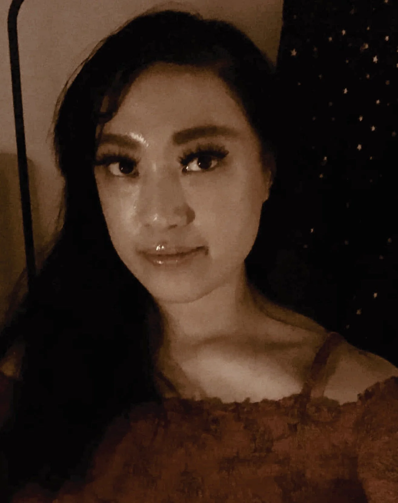 A woman with long dark hair wearing a brown top, with a dark background featuring star patterns.