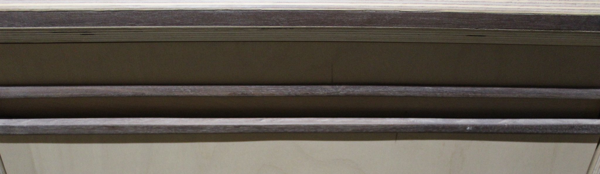 Close-up of a desk with dark wood surface and metal edge, underneath a beige wall.