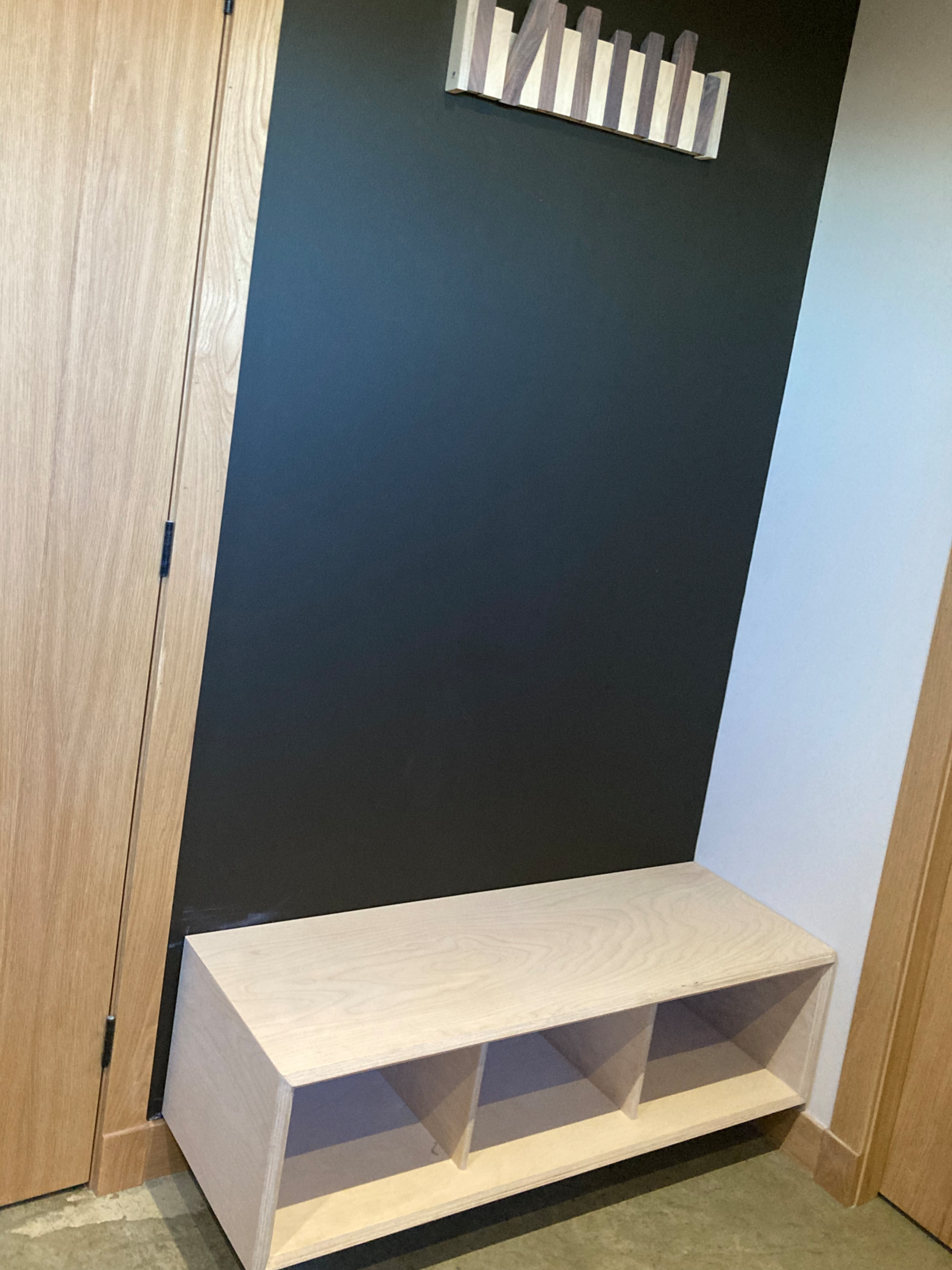 Modern entryway with a wooden bench with cubby compartments, a black accent wall, and a wooden wall art piece above the bench.