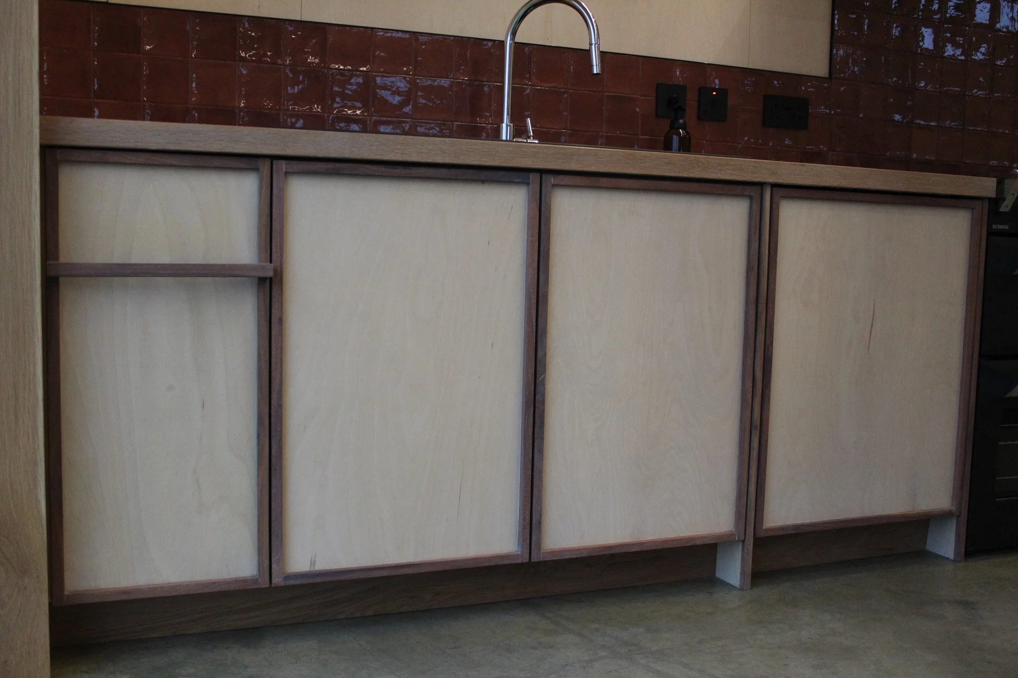 Kitchen countertop with a sink and a red backsplash, along with wooden cabinet doors.