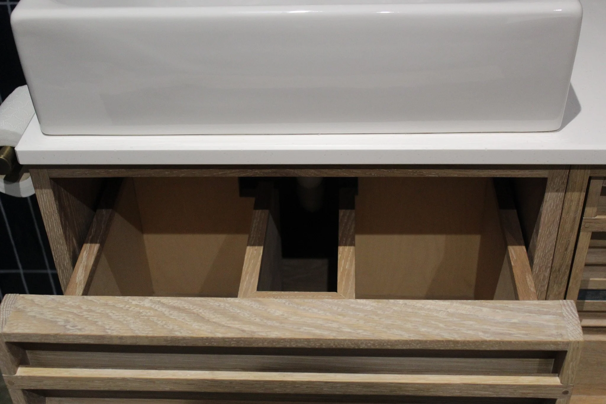 Open wooden drawer with empty compartments beneath a white countertop and a large white object on top.