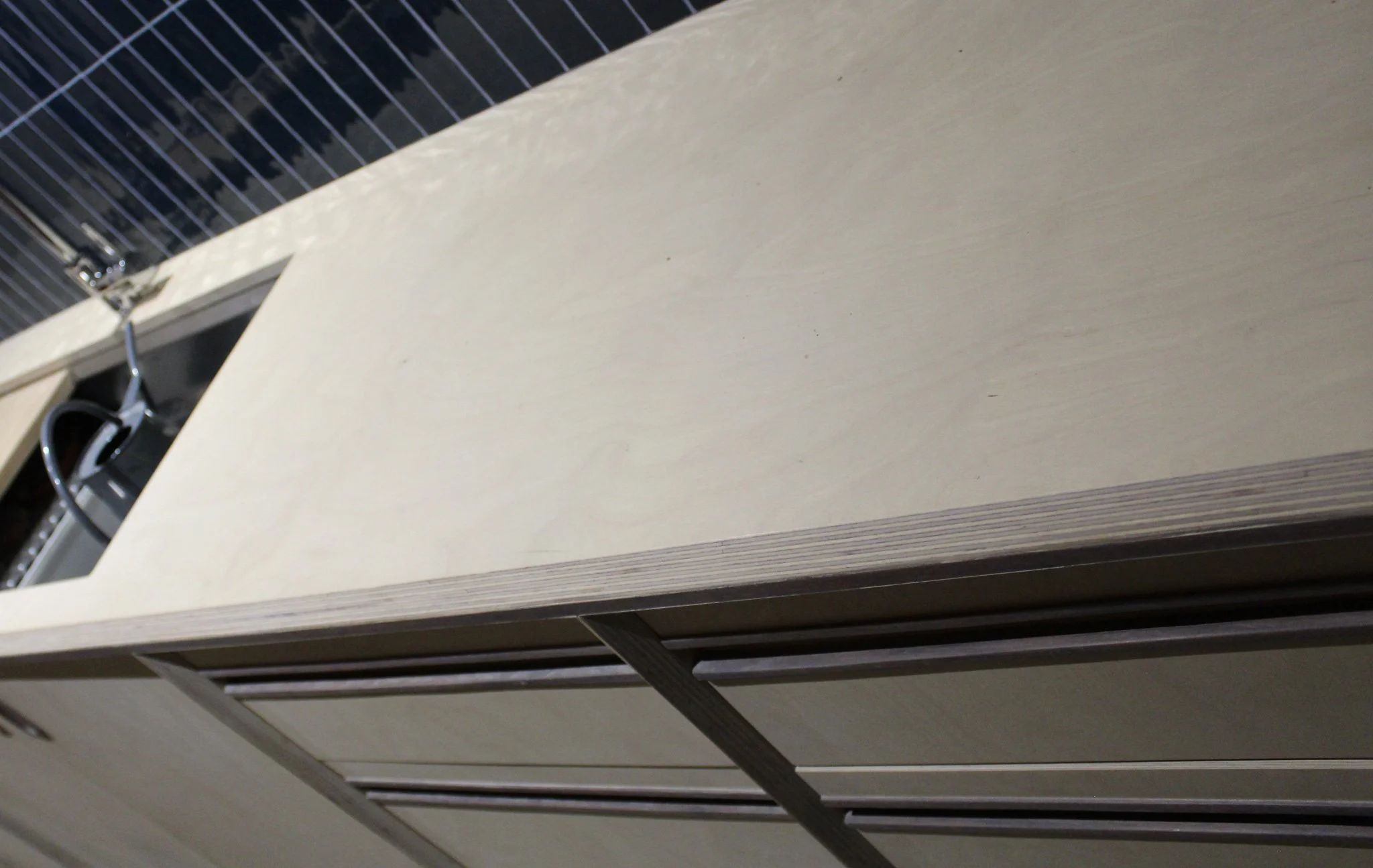 Close-up of a beige cabinet with metal trim and a dark countertop with a built-in sink and a faucet, viewed from a tilted angle.