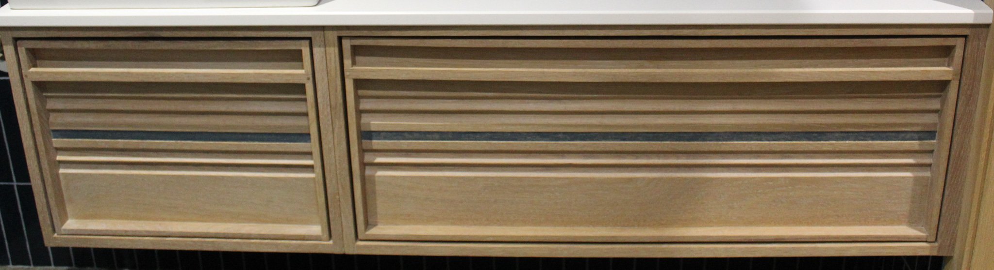 Wooden louvered cabinet with three drawers in a retail or display setting.