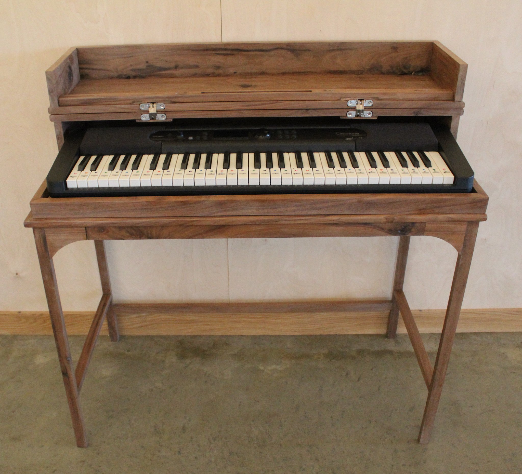 A wooden electronic keyboard stand with a digital keyboard on top, set against a beige wall.