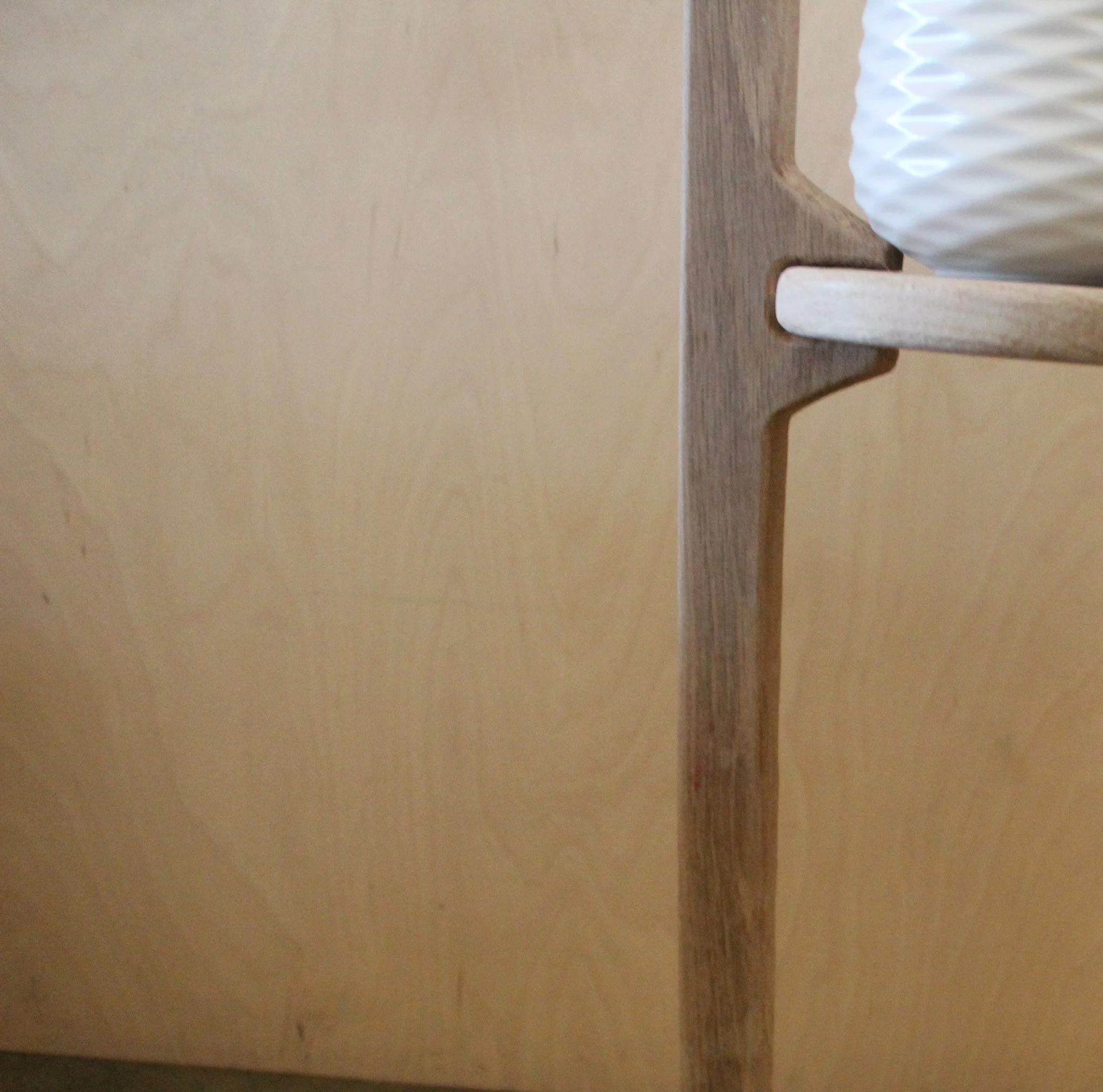 Close-up of a wooden plant stand with a decorative white ceramic vase on a wooden stand, partially visible on the right side.