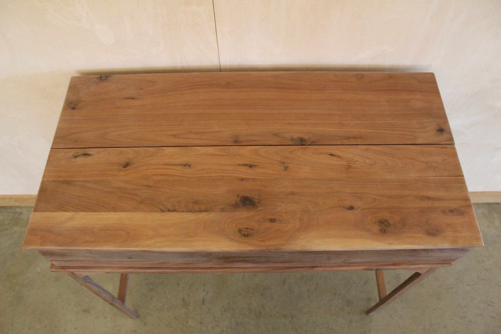 Top view of a wooden table with a slatted design and a natural wood finish, placed against a beige wall on a concrete floor.