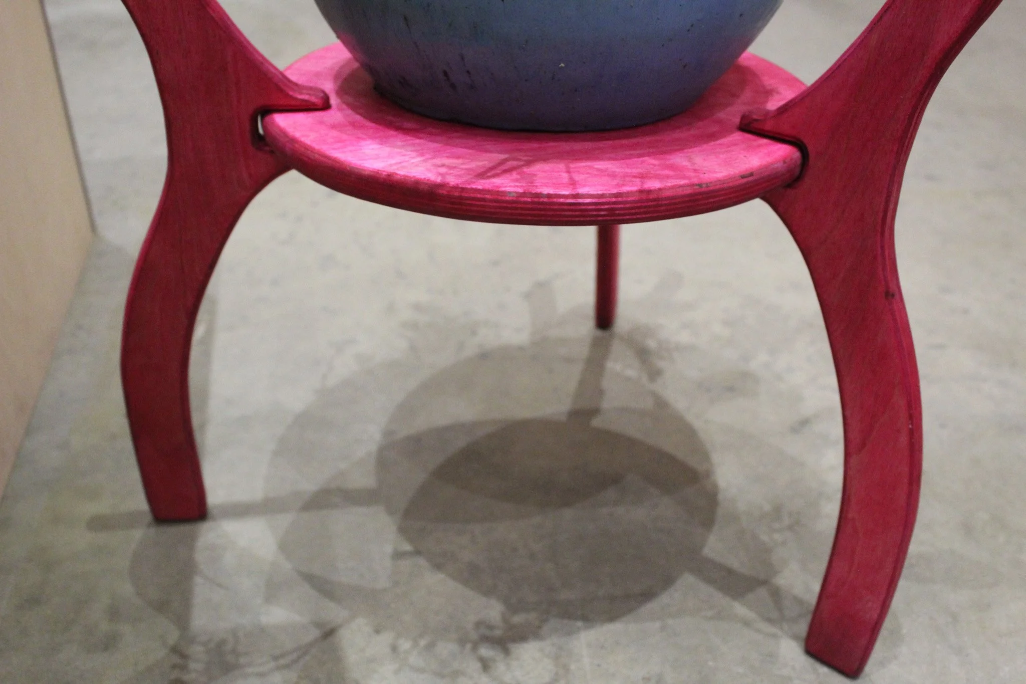 Close-up of a pink wooden plant stand and a shadow cast on the gray concrete floor.