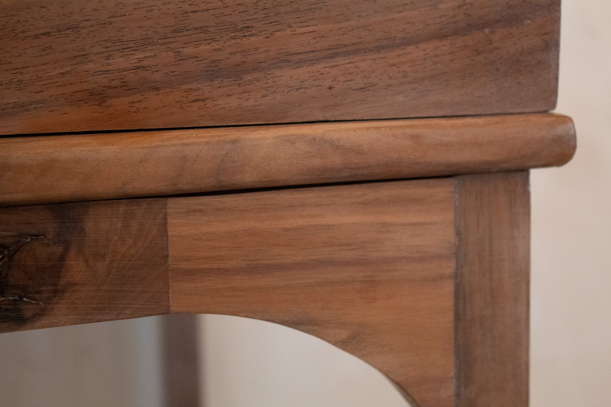 Close-up of a wooden piece of furniture showing the corner, drawer edge, and decorative leg with visible wood grain and smooth finish.