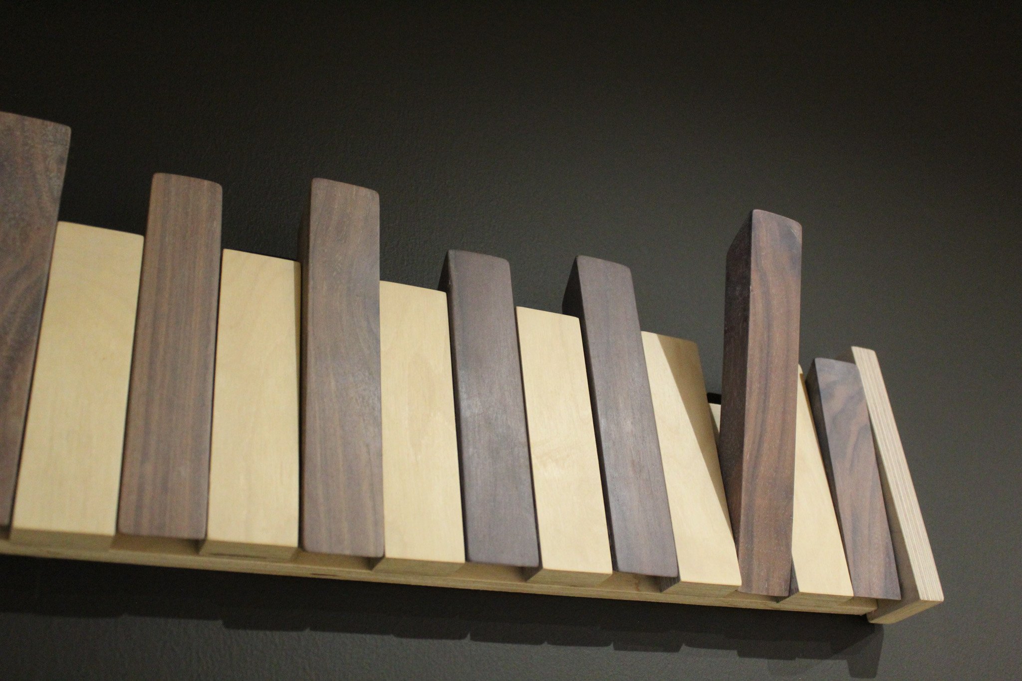 Close-up of a modern wooden piano coat hooks with alternating light and dark wood bars, on a dark background.