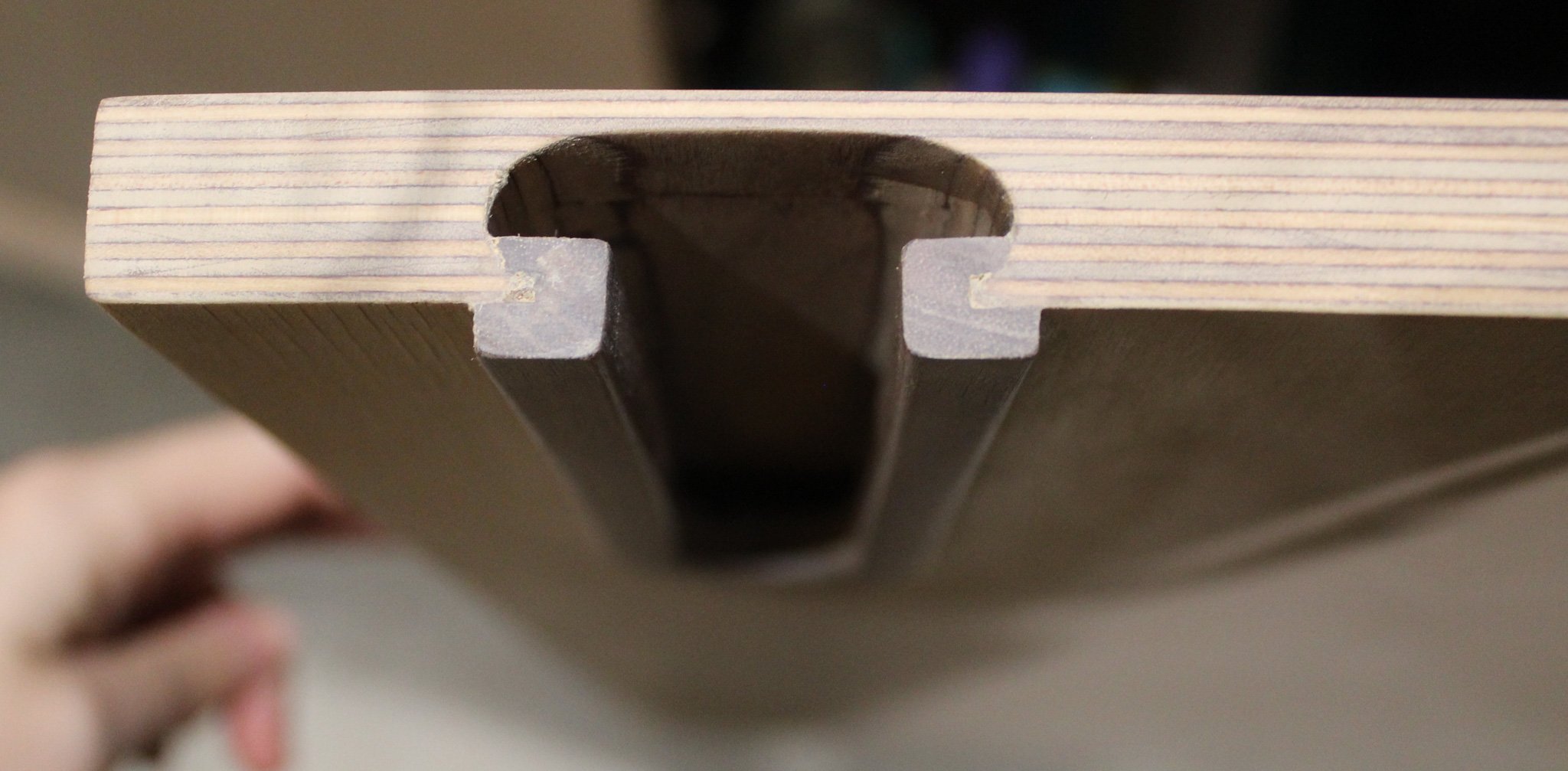 Close-up of a wooden table edge with a central metal T-slot groove.