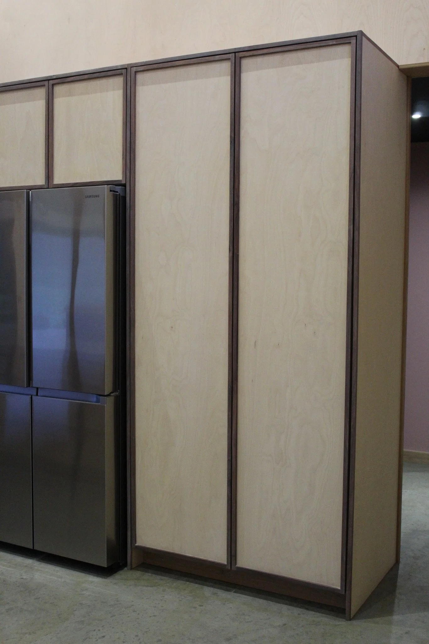 A wooden cabinet with three doors next to a stainless steel refrigerator in a kitchen.