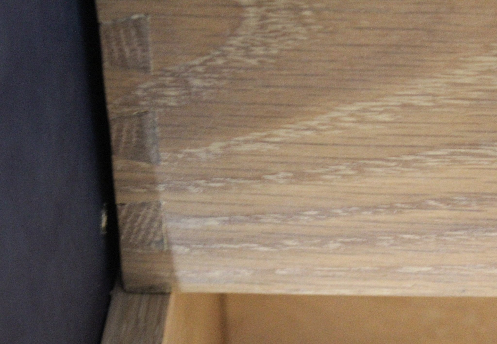 Close-up view of a corner of a wooden cabinet or furniture, showing the textured wood grain and edge details.