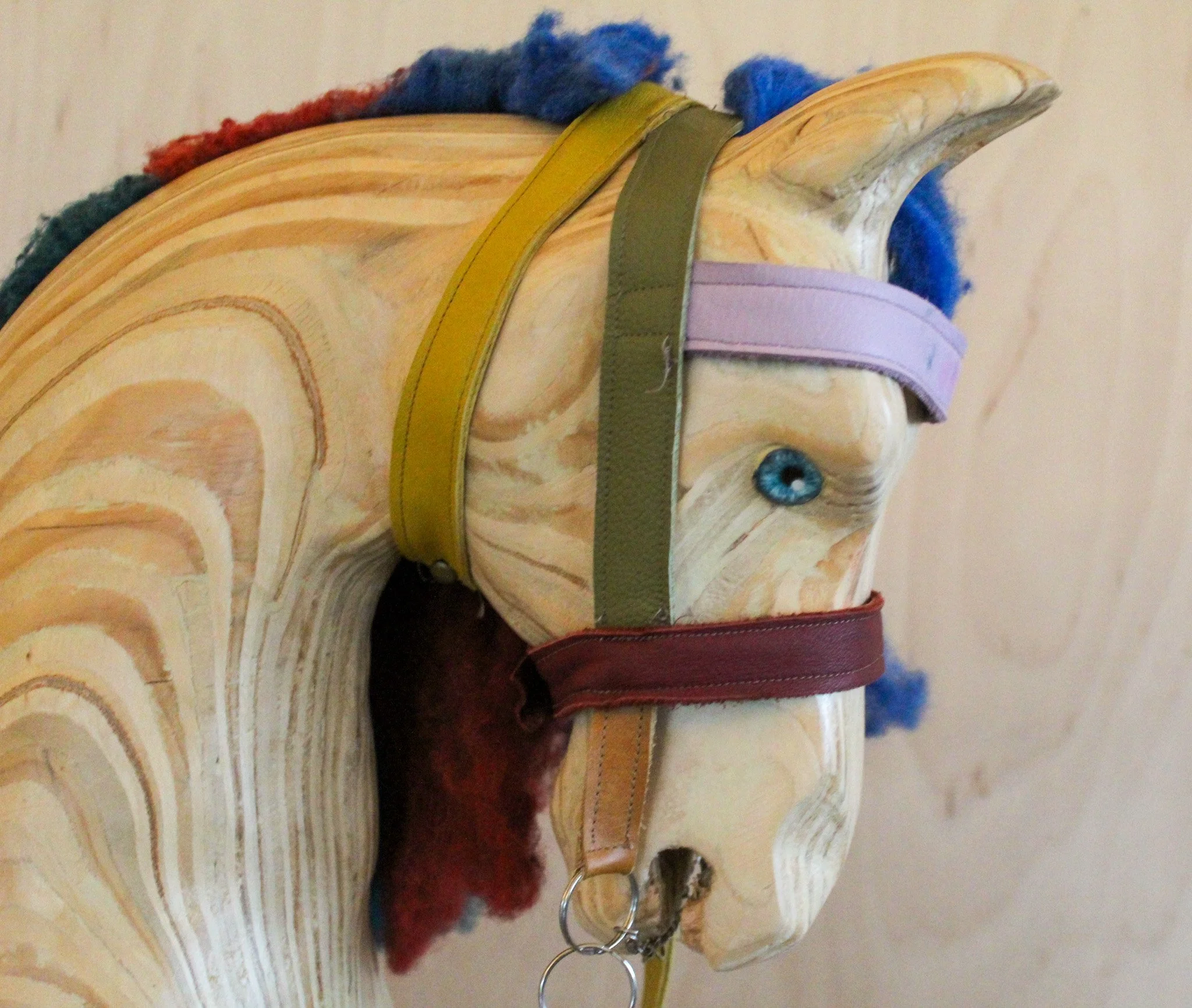 Wooden horse sculpture with colorful straps and a blue eye, decorated with multicolored yarn on its mane.