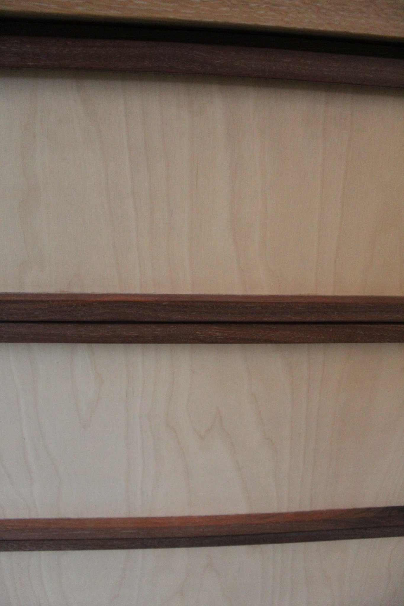 Close-up photo of beige and brown wooden drawer fronts with dark brown trim.