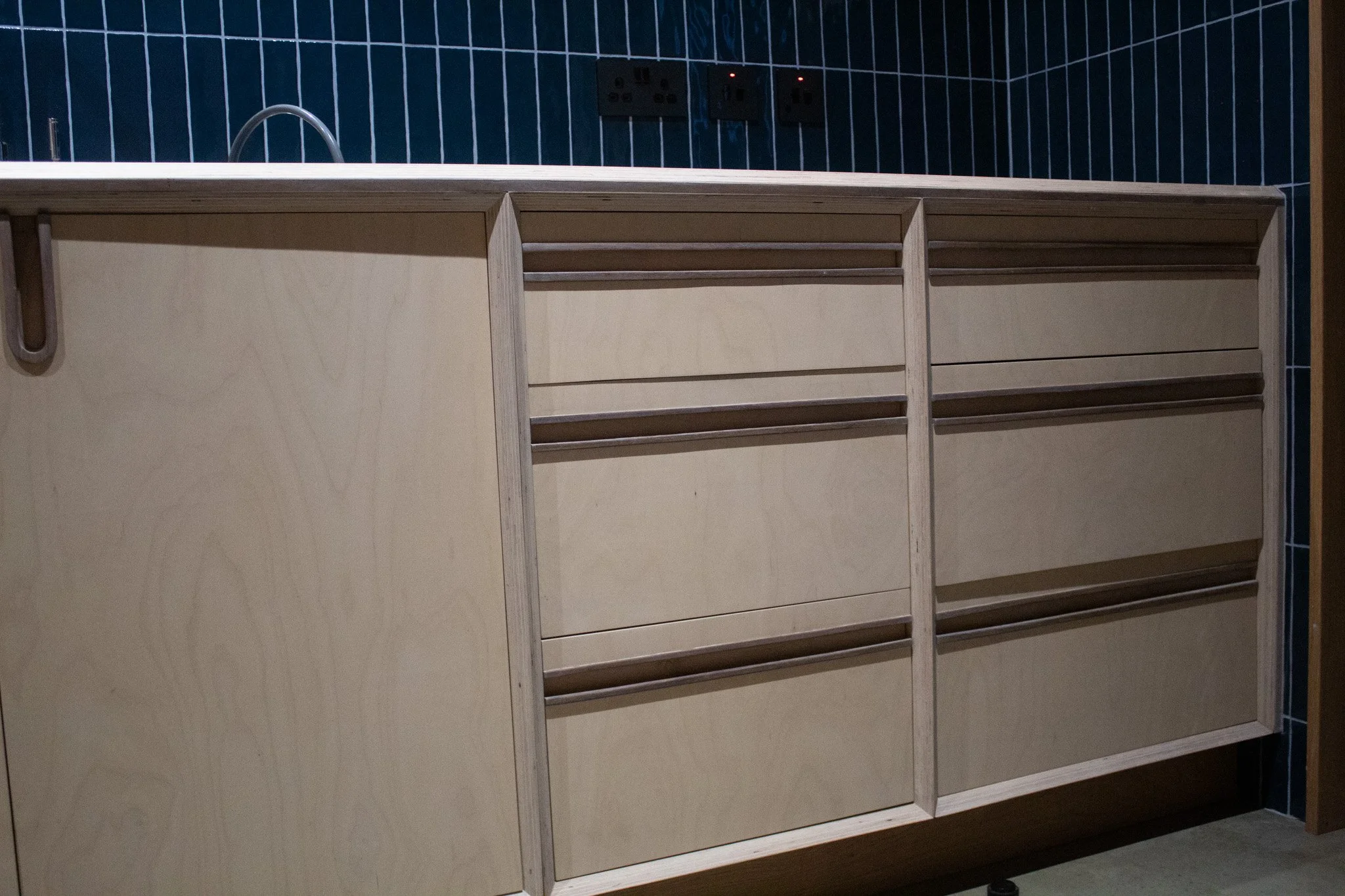 Wooden cabinet with multiple drawers and a countertop in a room with dark blue tiled walls.