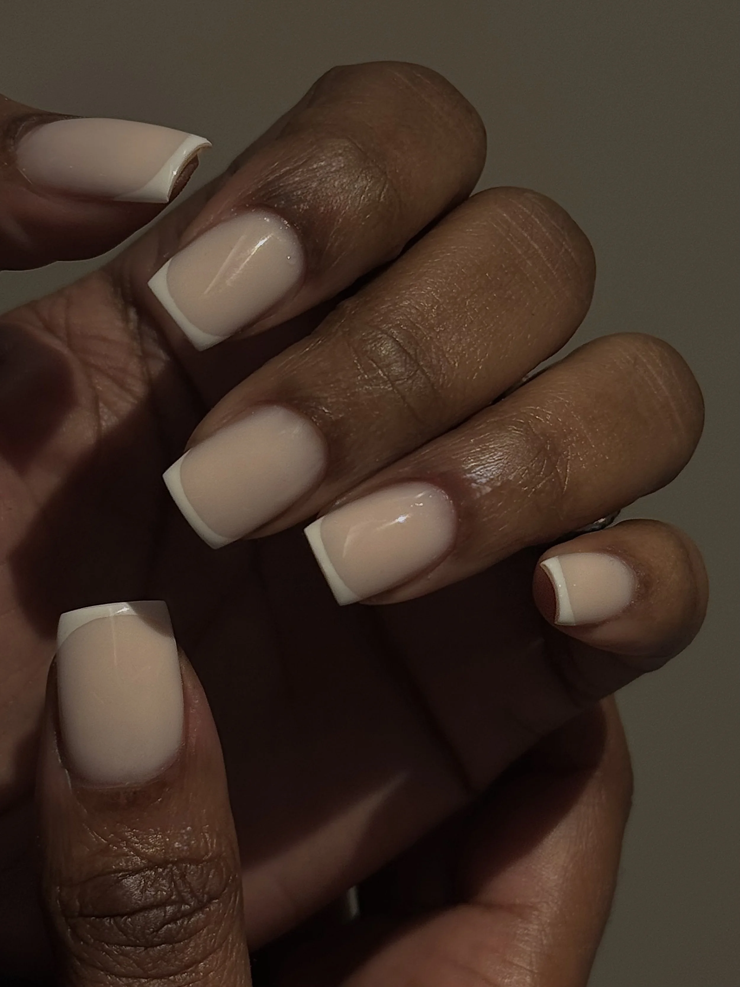 Close-up of dark-skinned hand with neatly manicured nails painted in a French manicure style, featuring natural pink nail bed with white tips.