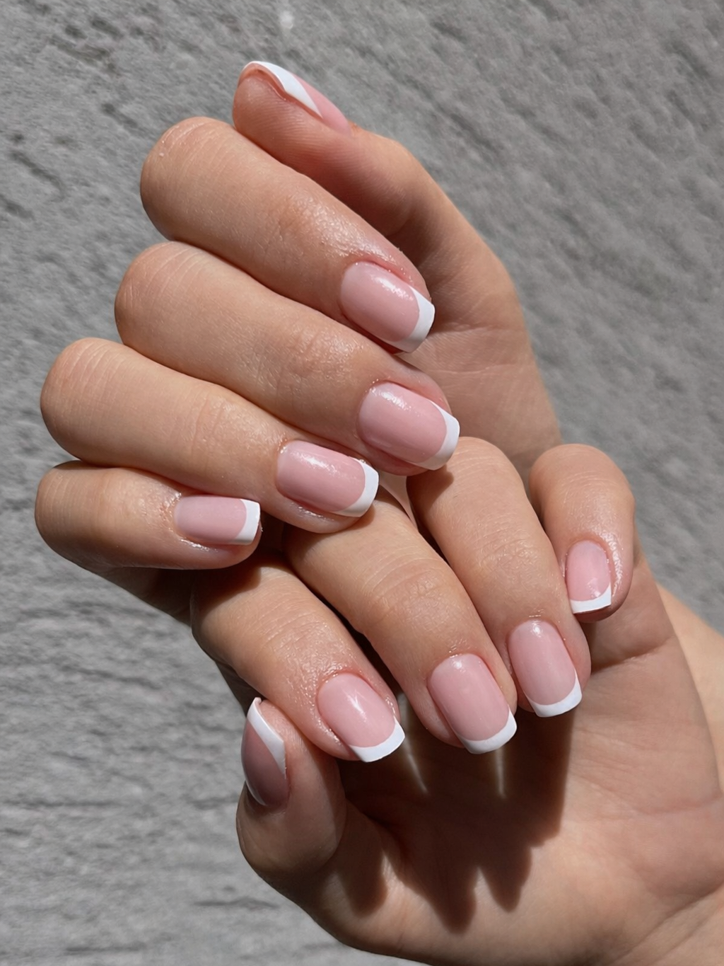 Close-up of a hand with neatly manicured nails featuring a classic French tip design, set against a textured gray background.