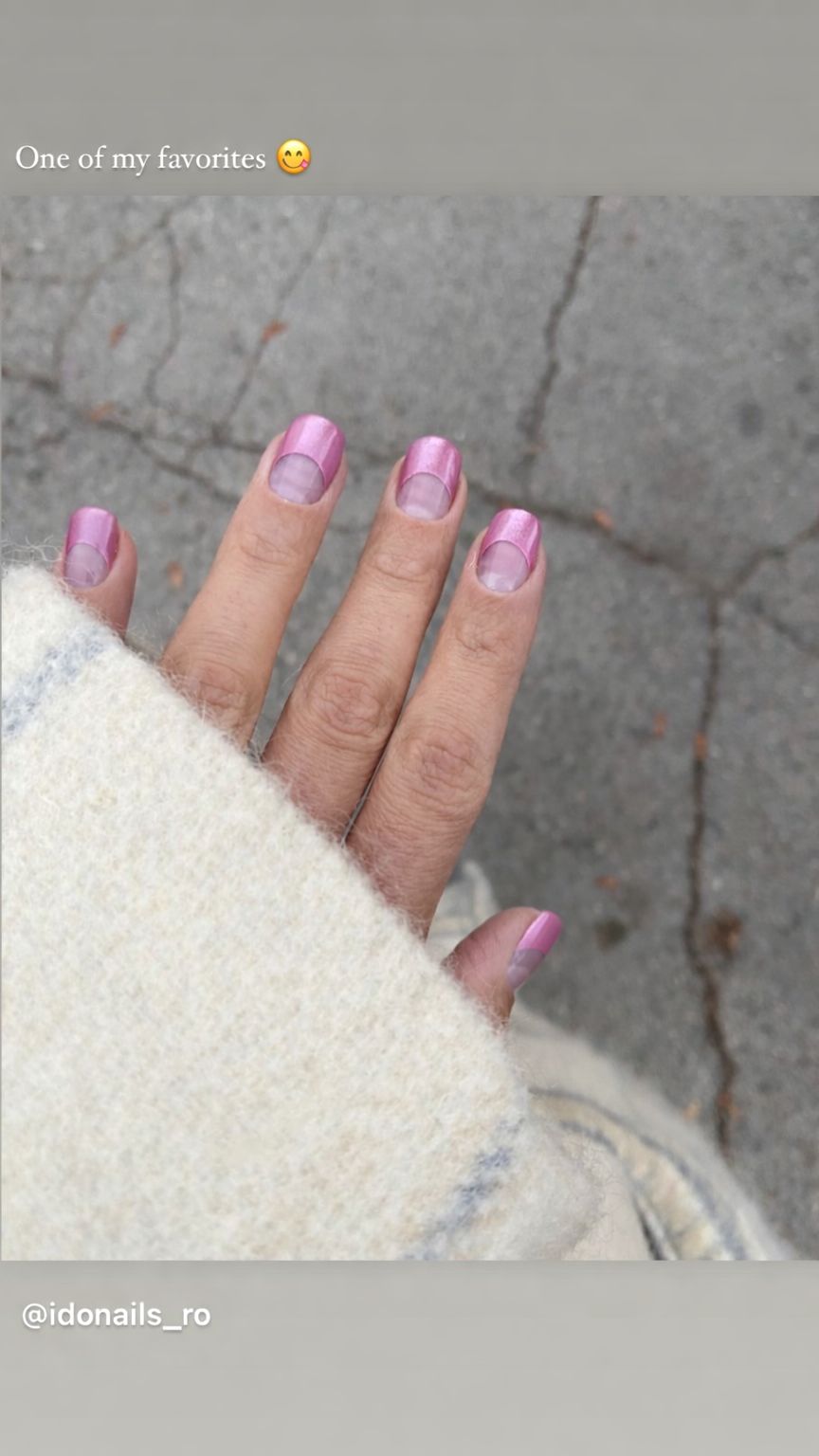 Close-up of a hand with pink French manicure nails, partially covered by a cream-colored fuzzy coat, against a cracked gray pavement background.