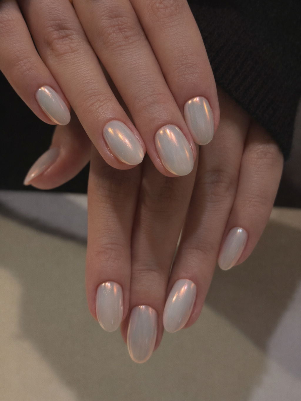 Close-up of hands with neatly manicured nails painted in a pearly, iridescent white color.
