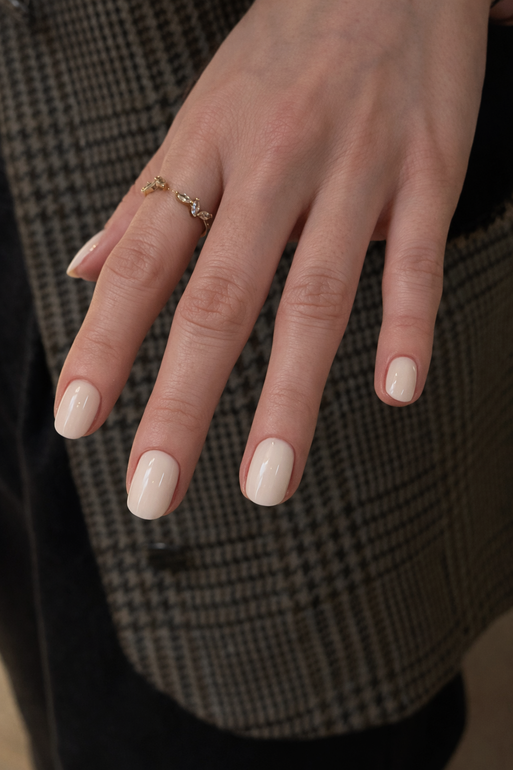 Close-up of a hand with manicured nails and a gold ring featuring small diamonds, set against a patterned fabric background.