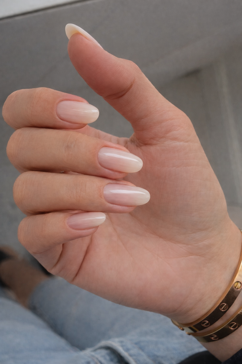 Close-up of a hand with neatly manicured, light pink, almond-shaped nails, wearing a brown leather bracelet with metallic studs.