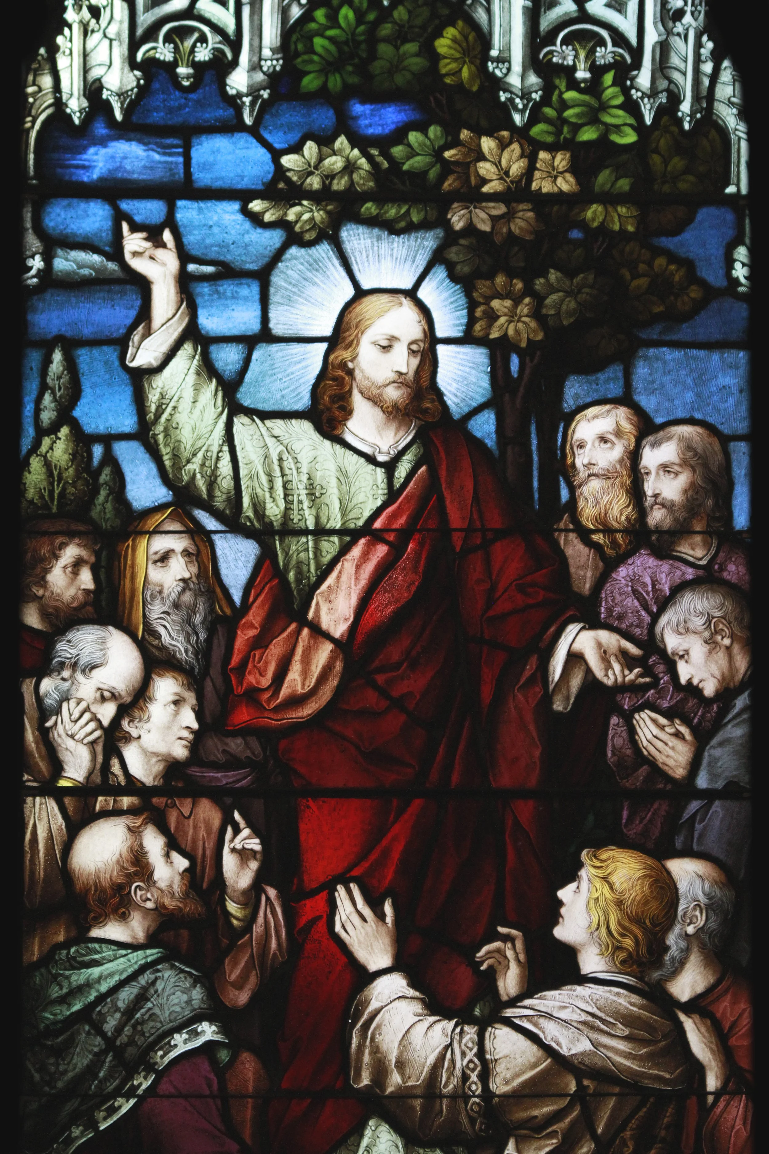 Colorful stained glass window depicting Jesus Christ surrounded by his disciples, with one disciple pointing towards Jesus.