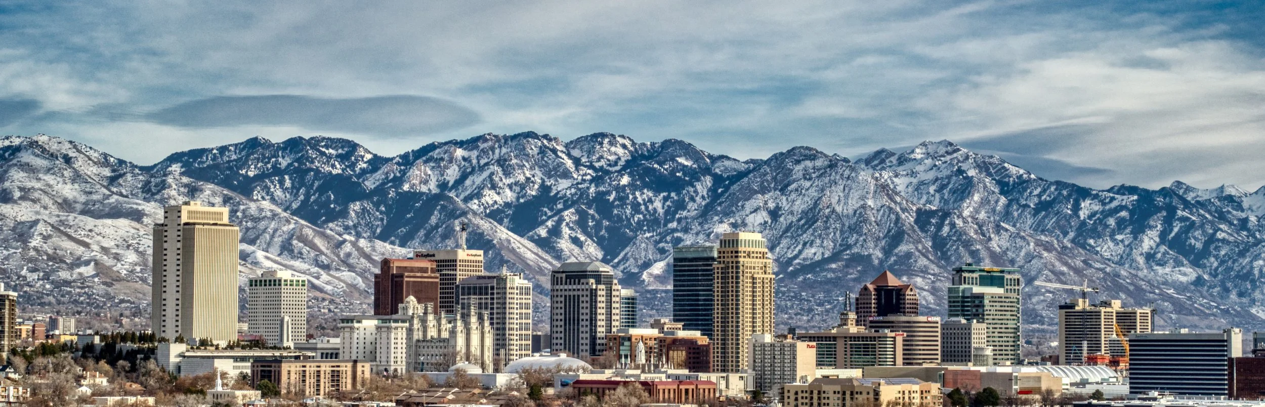 City skyline with tall buildings and snow-covered mountains in the background.