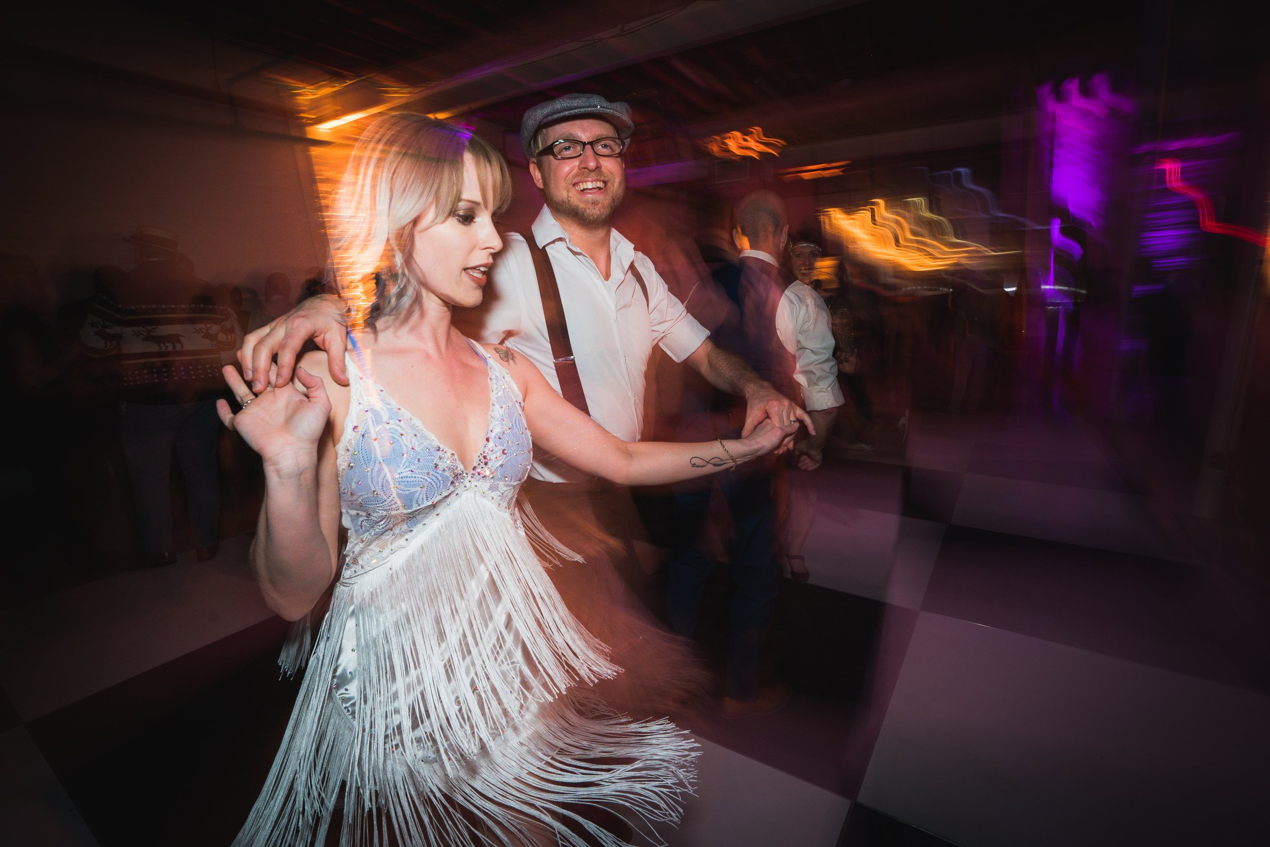 Couple dancing at a party with colorful lighting effects.