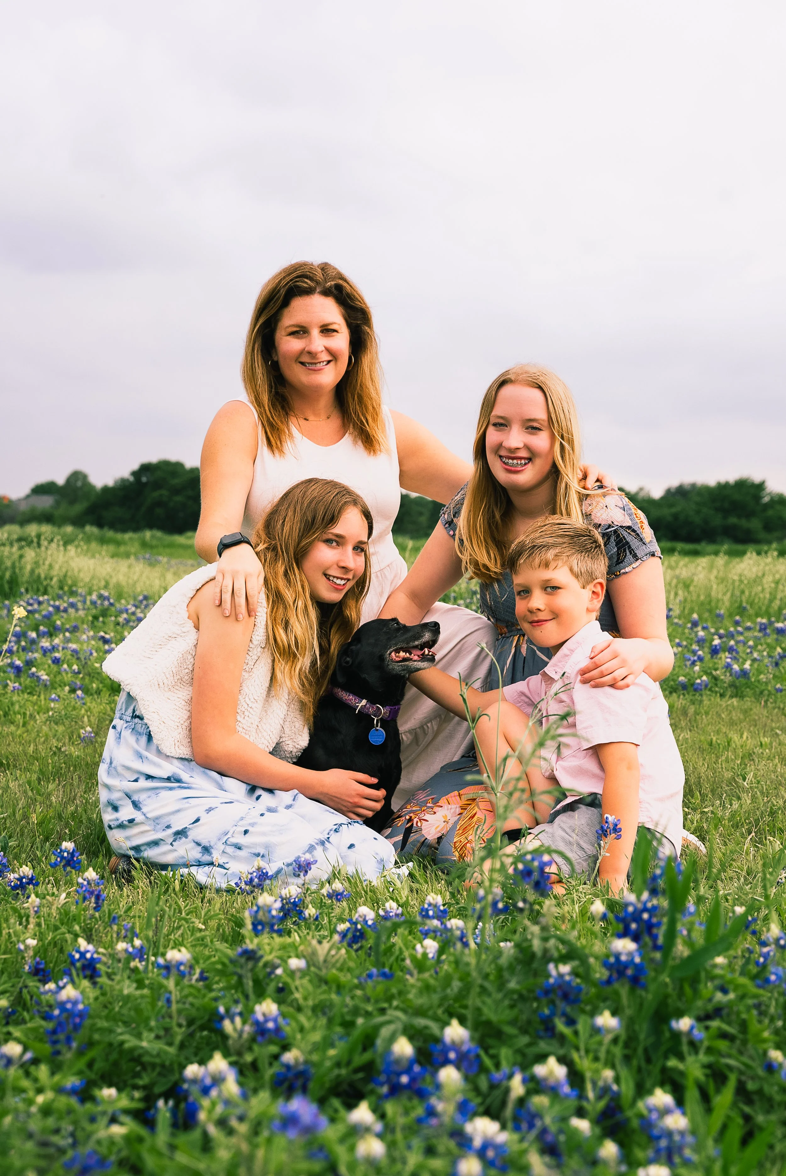 Family of four with a dog in a field of blue flowers during daytime.