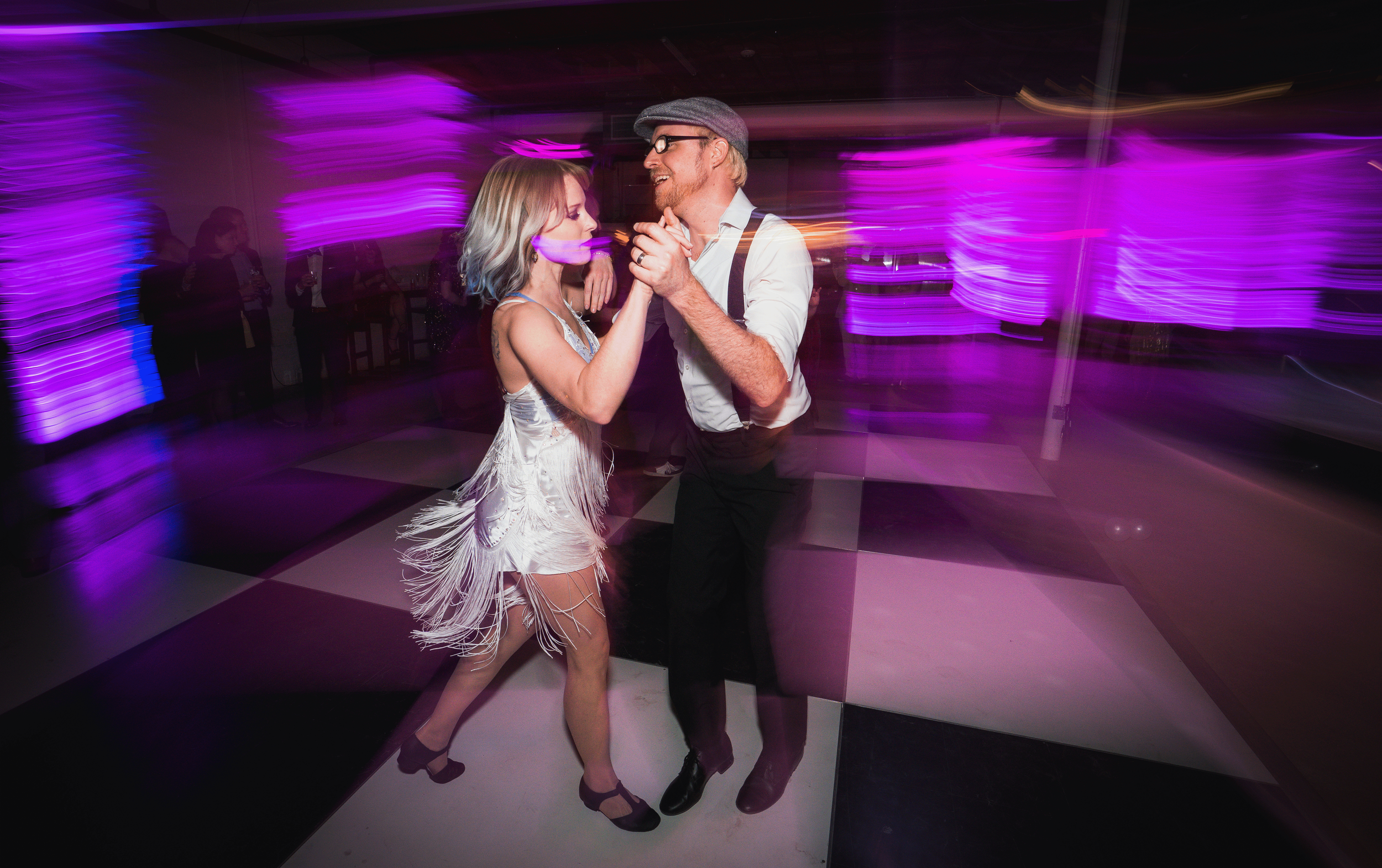 A couple dancing together on a checkered dance floor with purple lighting effects in the background.