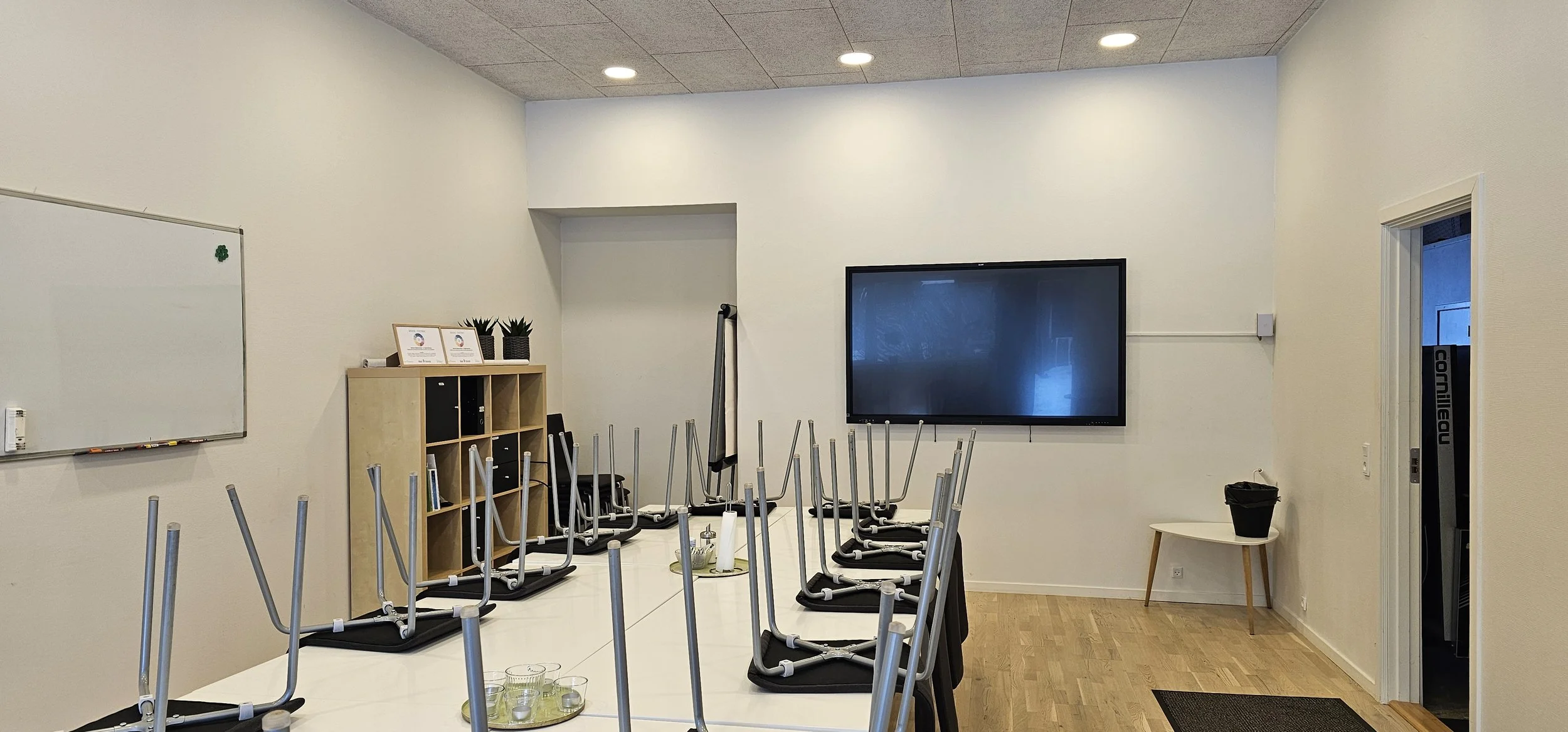 Et mødelokale med storskærm på væggen og borde med stole, der er vendt op og ned.