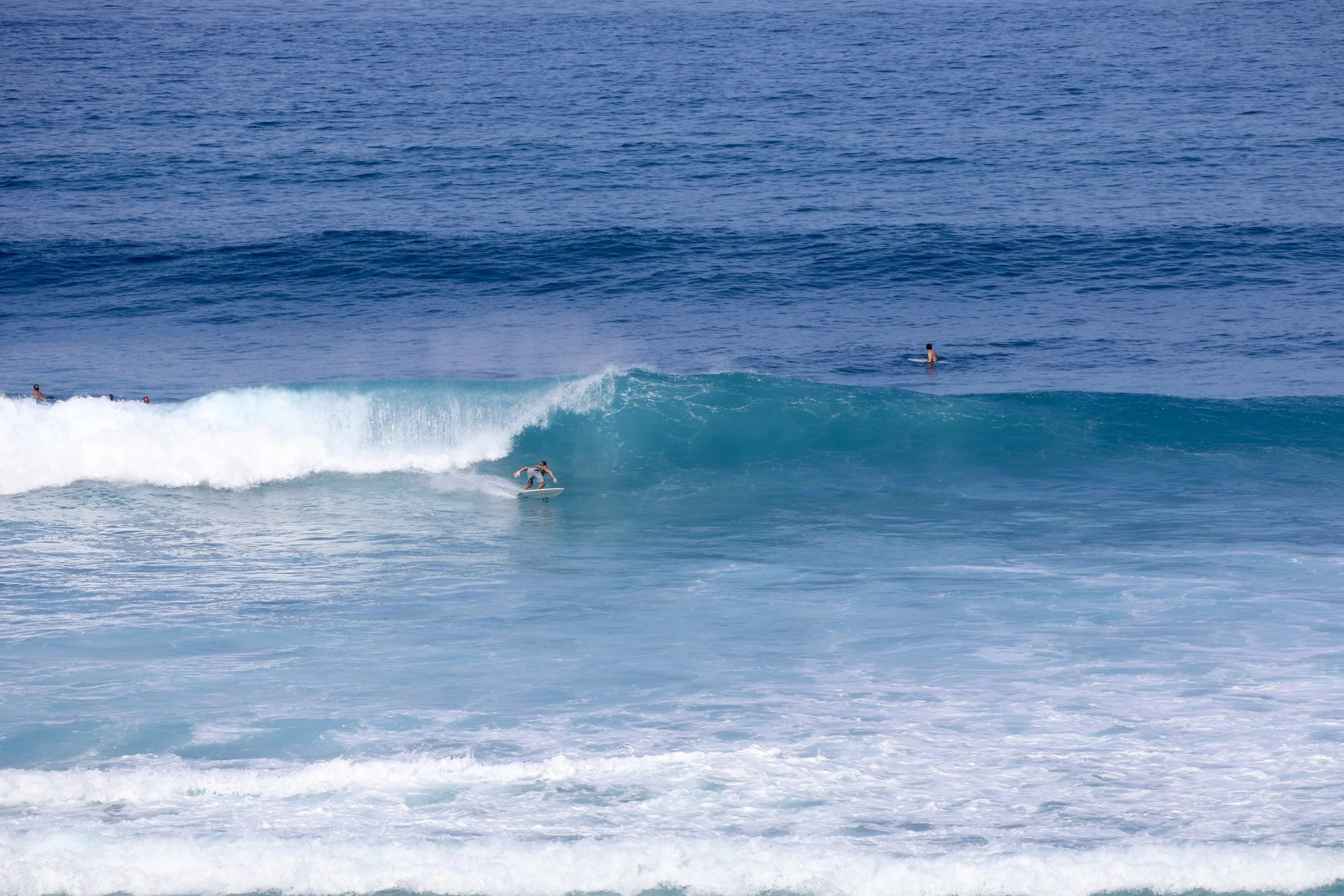 A person surfing on a wave in Uluwatu with other people swimming and standing in the water in the background.