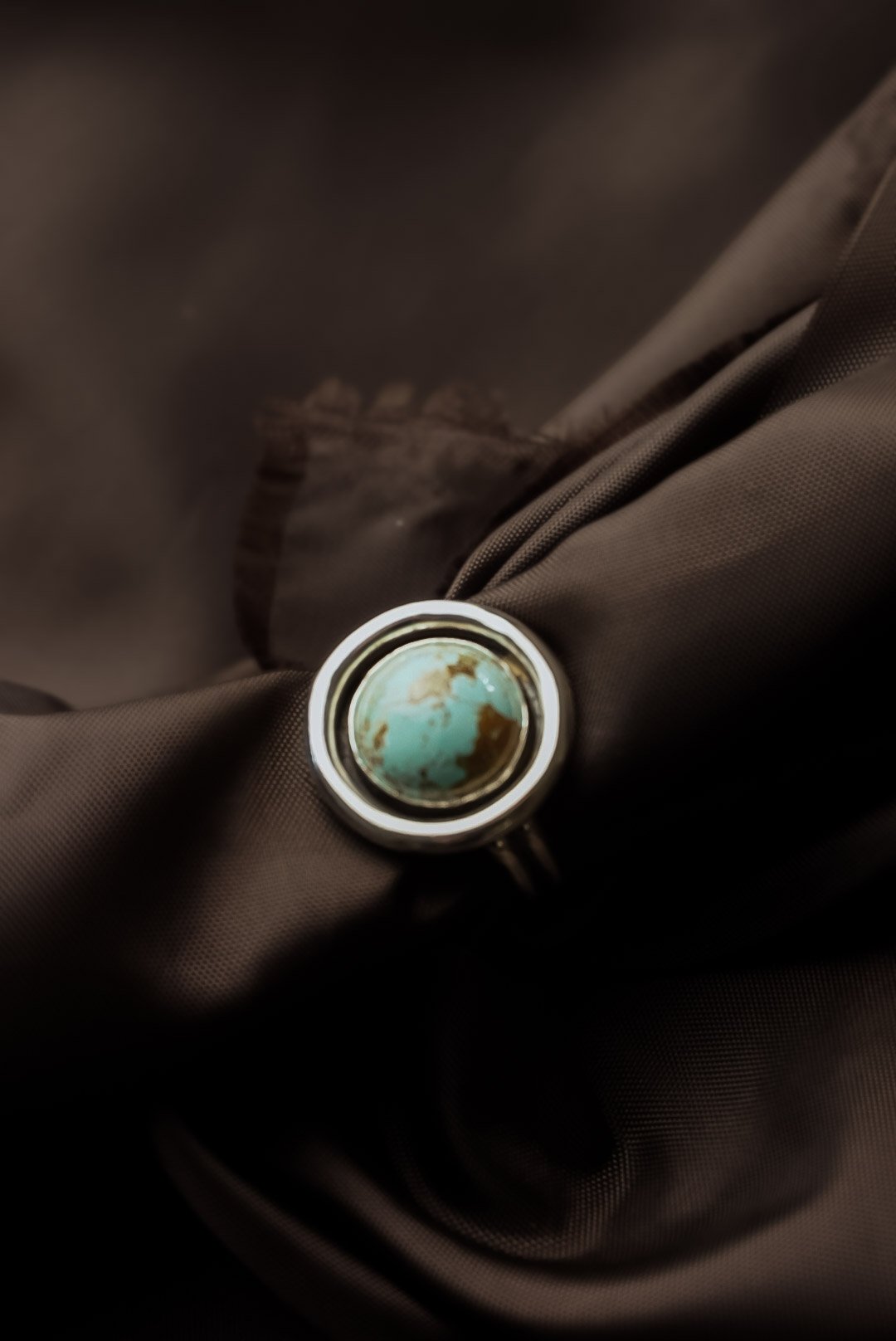 Close-up of a ring with a turquoise and brown stone, resting on a dark fabric background.