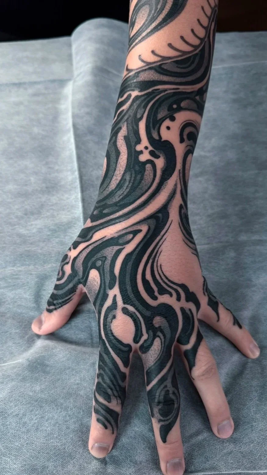A person's hand and arm with an intricate black and pink tattoo design covering them.