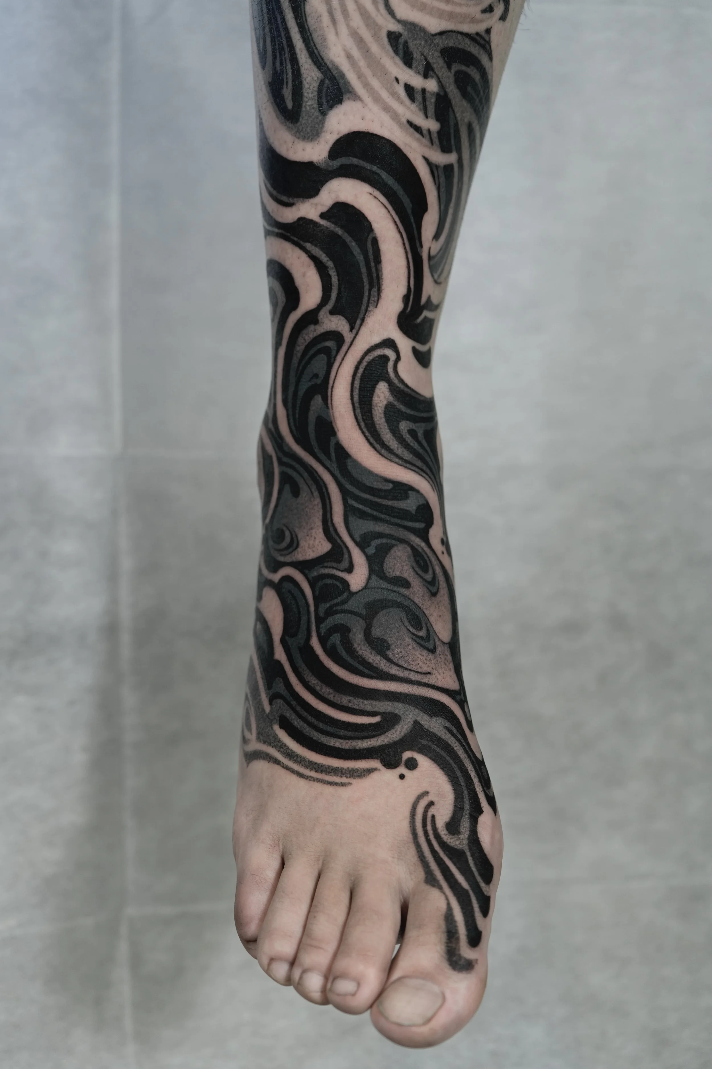 A close-up of a person's arm and hand, featuring a black and pink abstract swirl tattoo covering the forearm and extending to the wrist and hand, against a plain background.